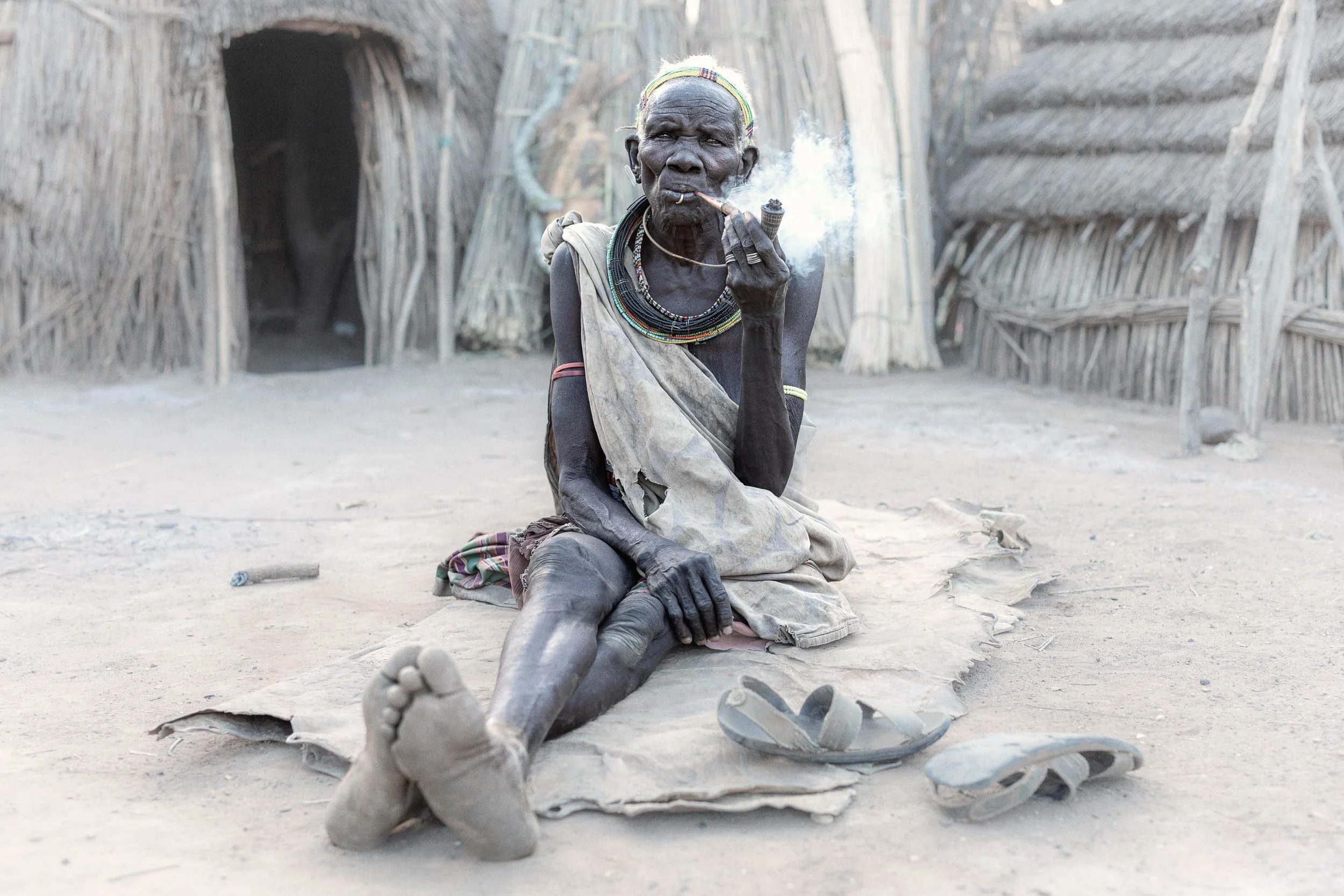 Old woman sitting on ground smoking pipe, South Sudan