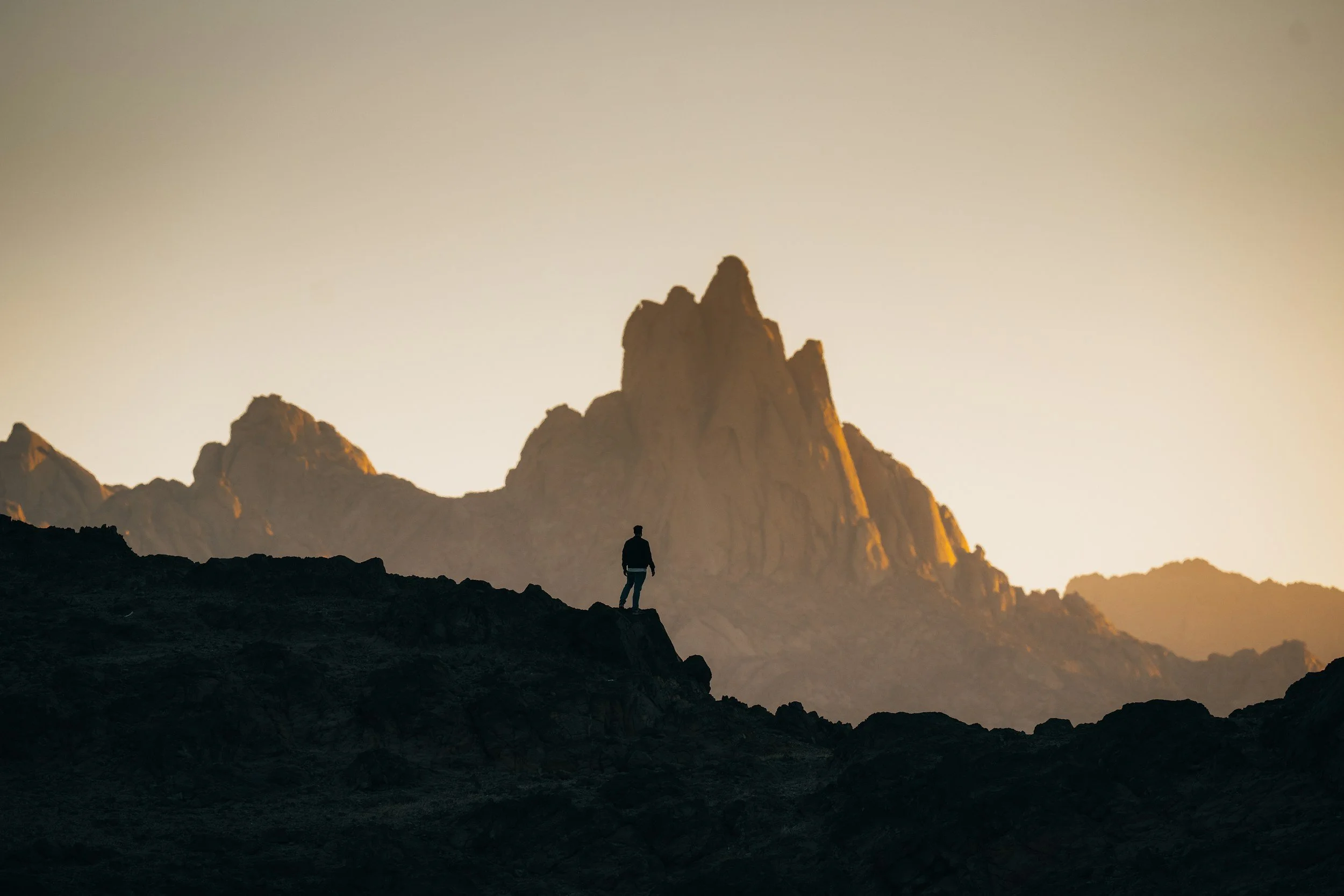 Silhouette of a woman standing alone on a rocky mountain peak at sunset — representing the courage it takes to do the inner work of conflict transformation
