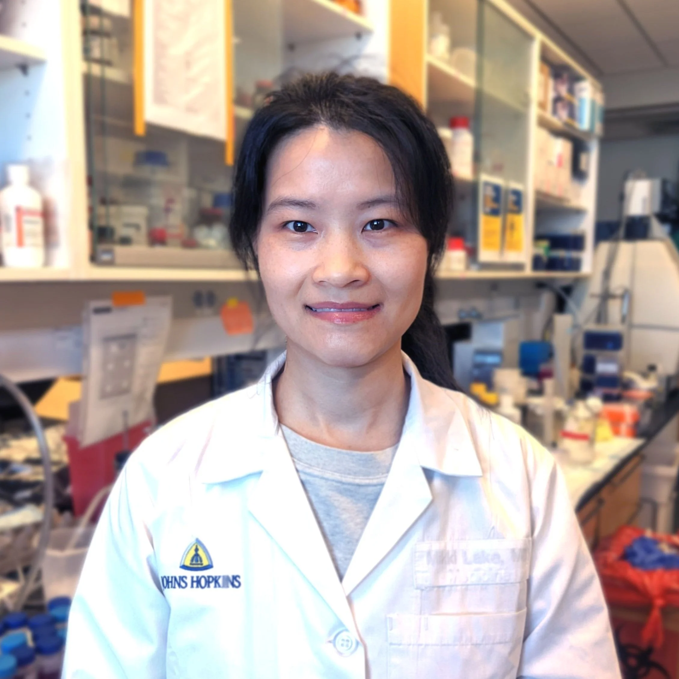 A woman in a lab coat standing in a laboratory filled with scientific equipment and supplies.
