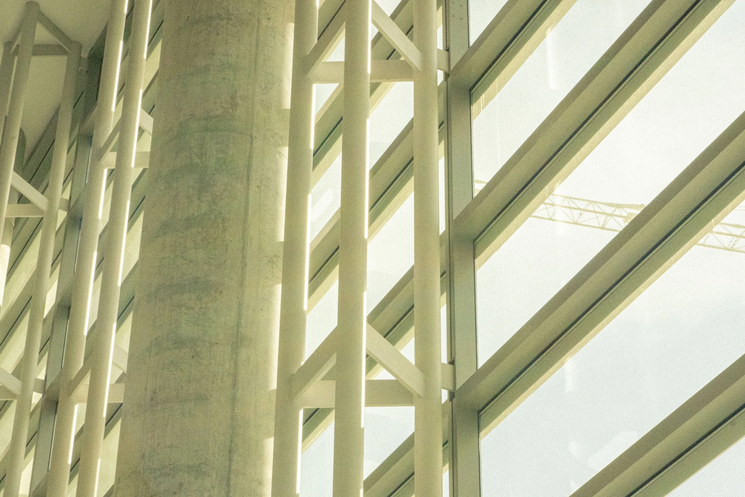 Close-up of the modern architectural interior with large vertical concrete column, white structural beams, and pink-tinted glass windows letting in natural sunlight.