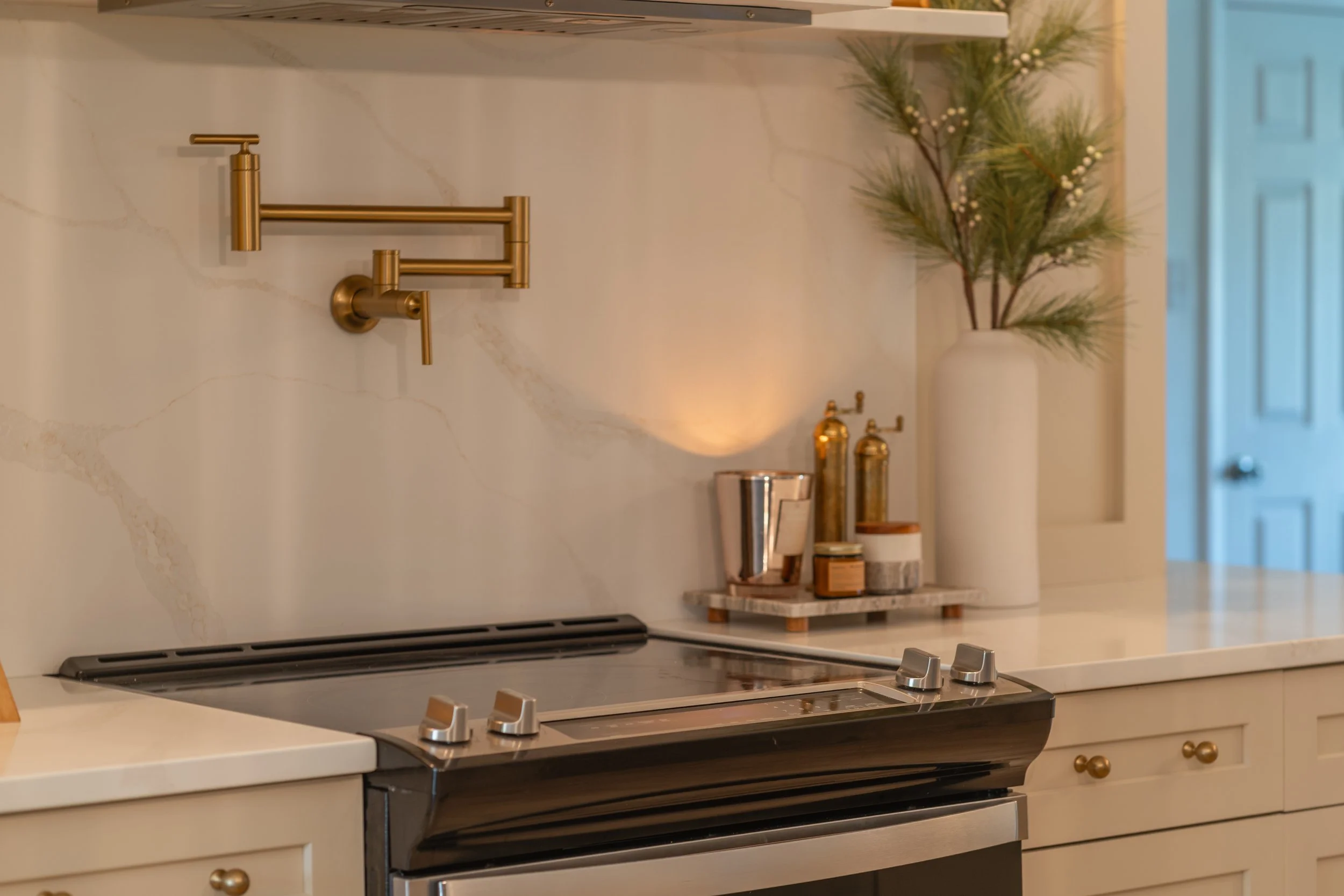 Modern kitchen with marble backsplash, wall-mounted brass faucet, stovetop, and decorative vases with greenery.