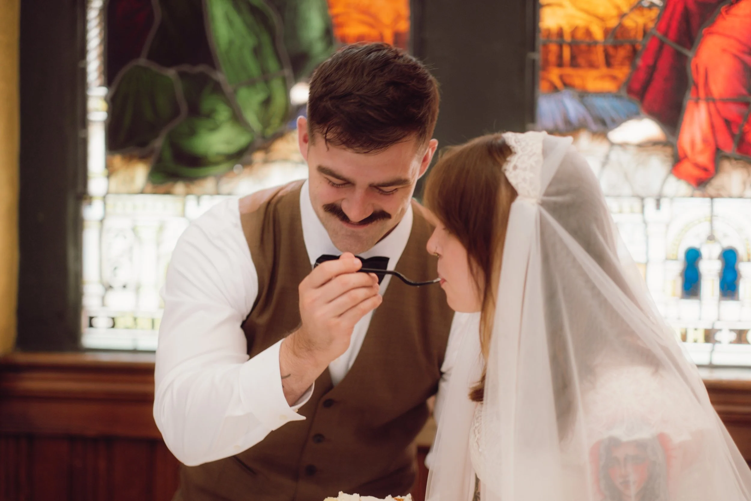 Groom feeds bride cake in front of stained glass windows at Sacred Heart Cultural Center wedding in Augusta, Georgia