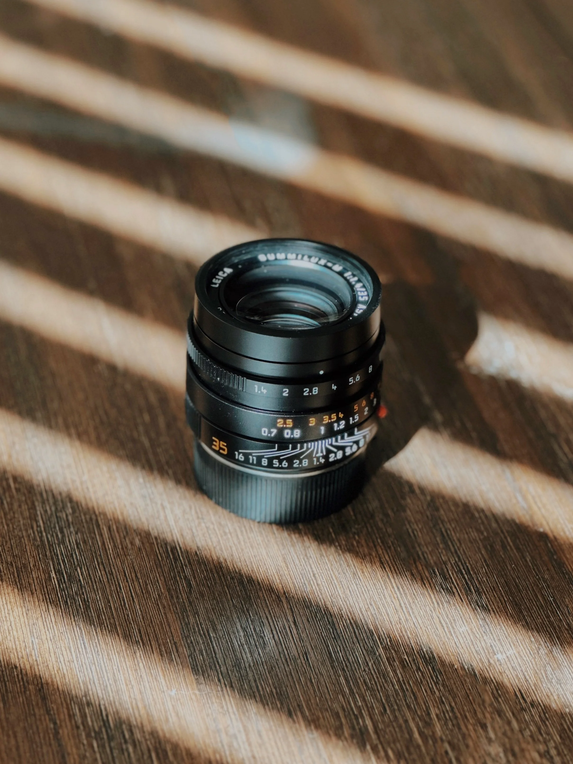 Leica Summilux 35mm f/1.4 ASPH lens on a wooden table in striped window light