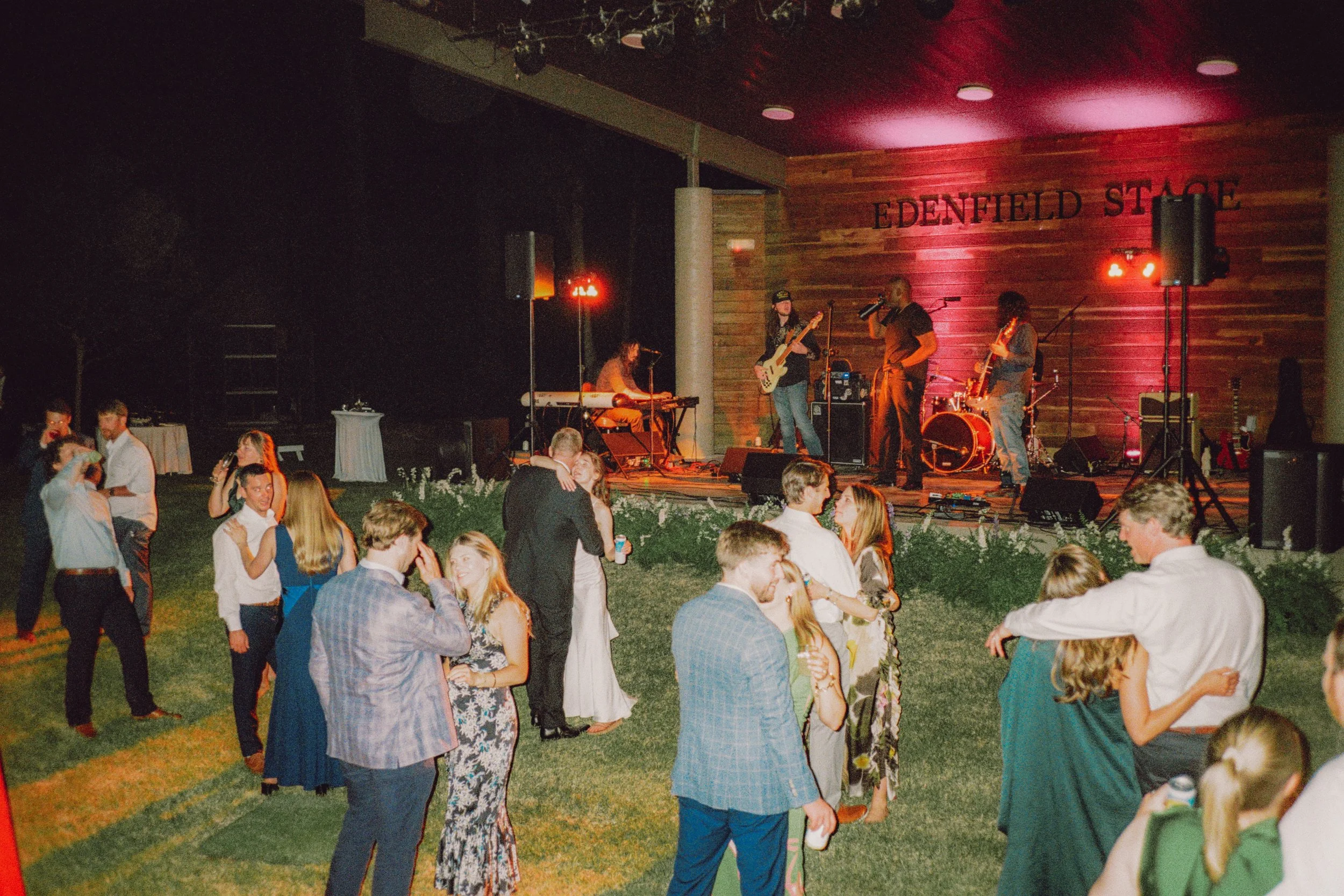 Wedding guests dancing on the lawn at night while a live band plays on an outdoor stage in Macon