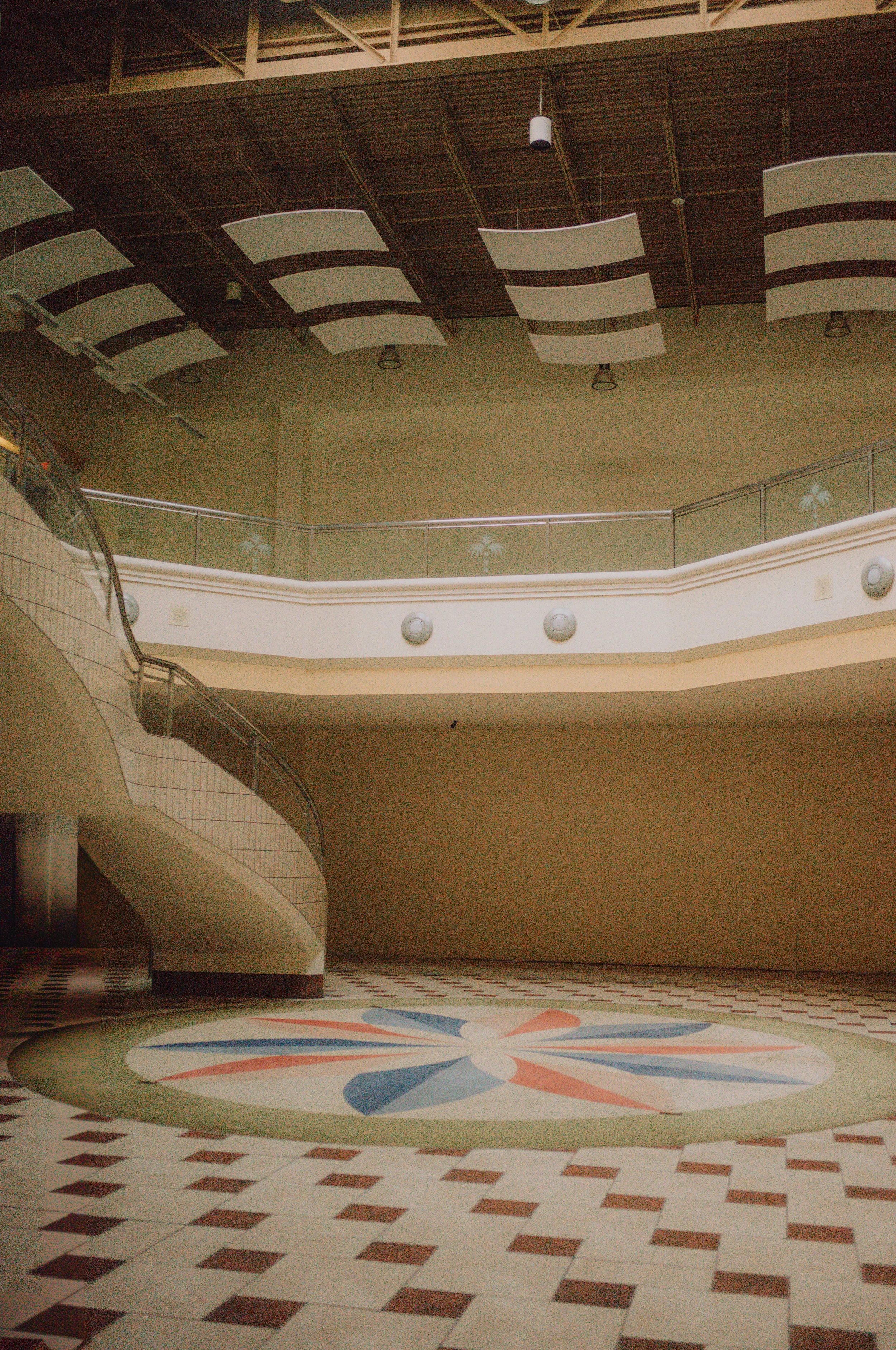 Interior of an empty shopping mall in Columbia, South Carolina (Columbia Place Mall) with tiered floors, a circular decorative design on the tiled floor, and suspended panels on the ceiling.
