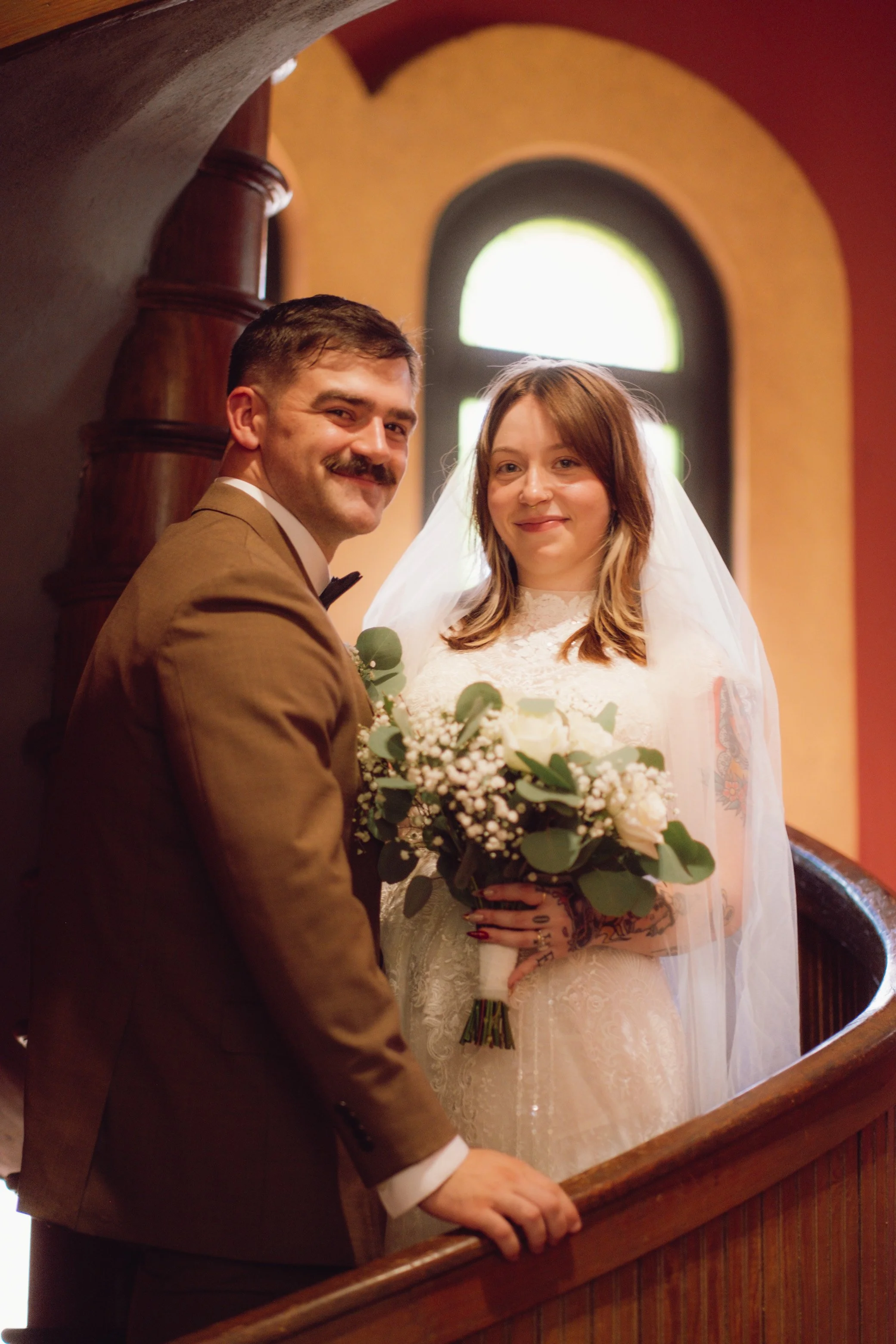 A bride and groom standing on a staircase inside a church, smiling at the camera during their wedding.
