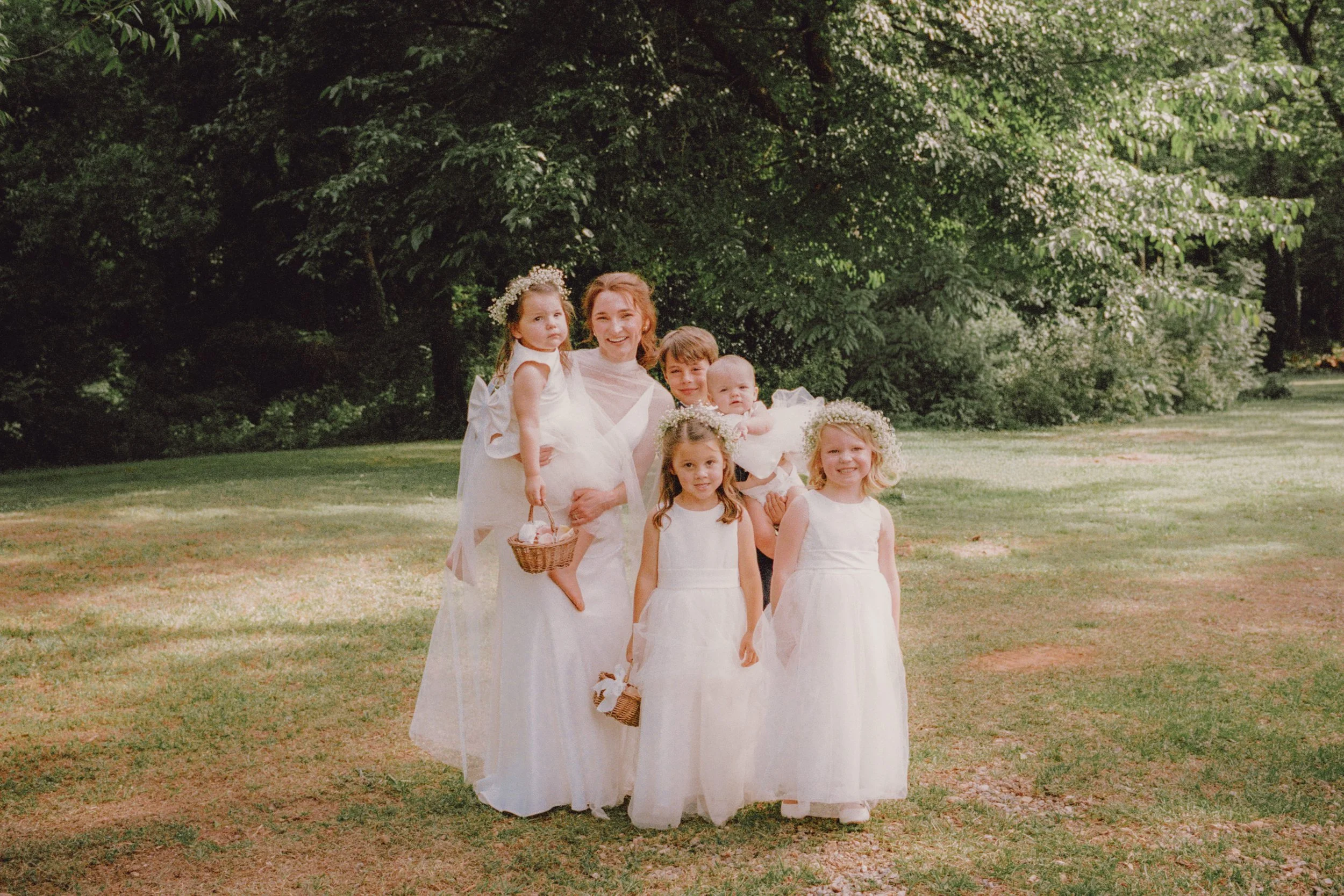 Bride in a sheer cape veil surrounded by flower girls in white dresses in an open field at a spring wedding in Macon, GA