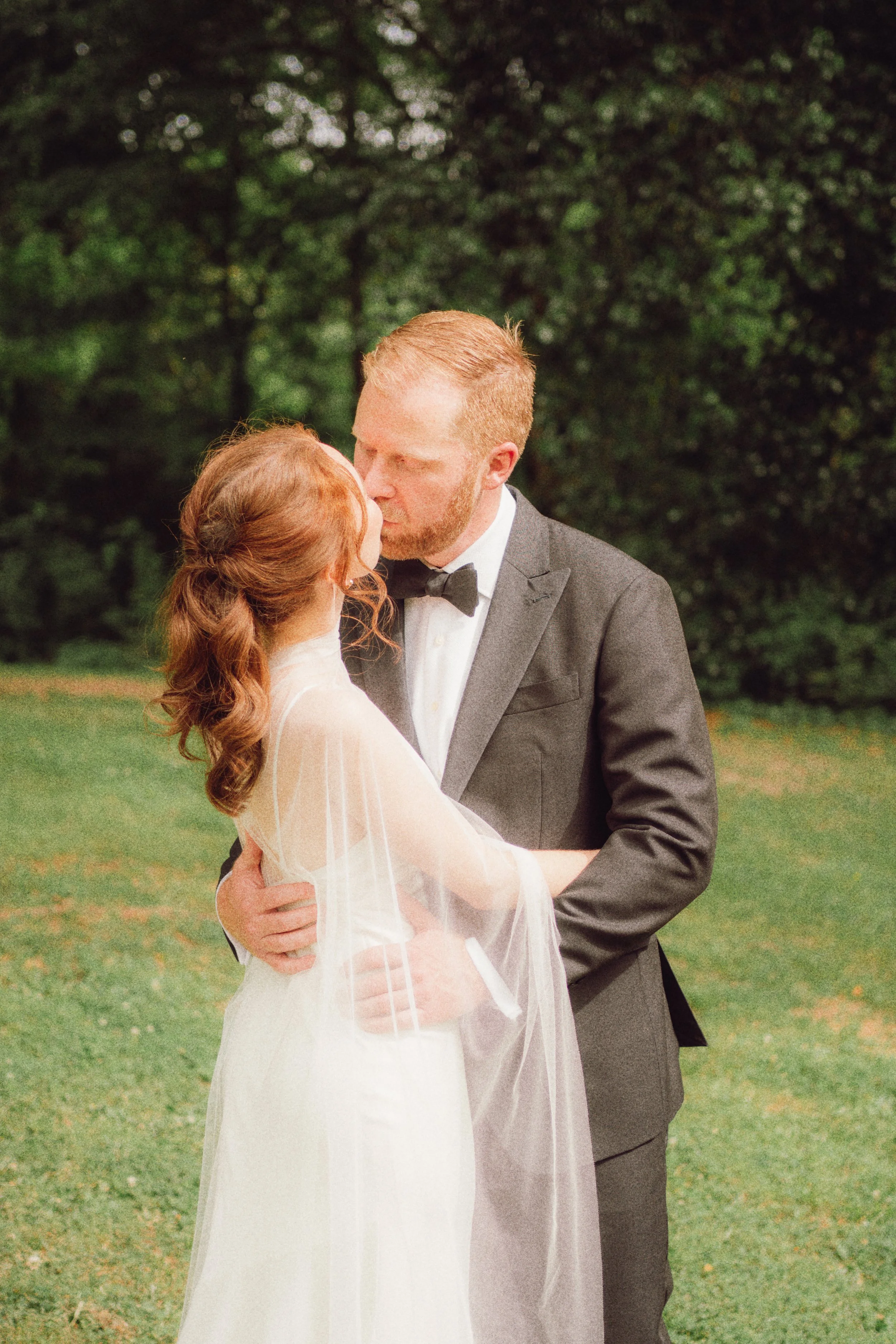 Bride and groom kissing in front of deep green trees during their first look at the Museum of Arts and Sciences in Macon, Georgia