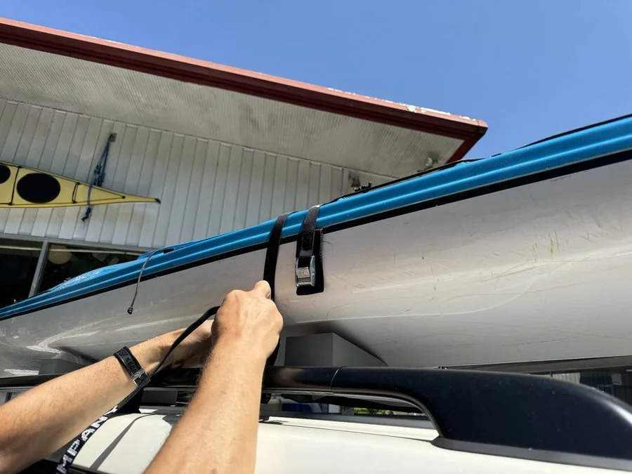 man secures kayak with cam straps on foam pads on SUV roof rack