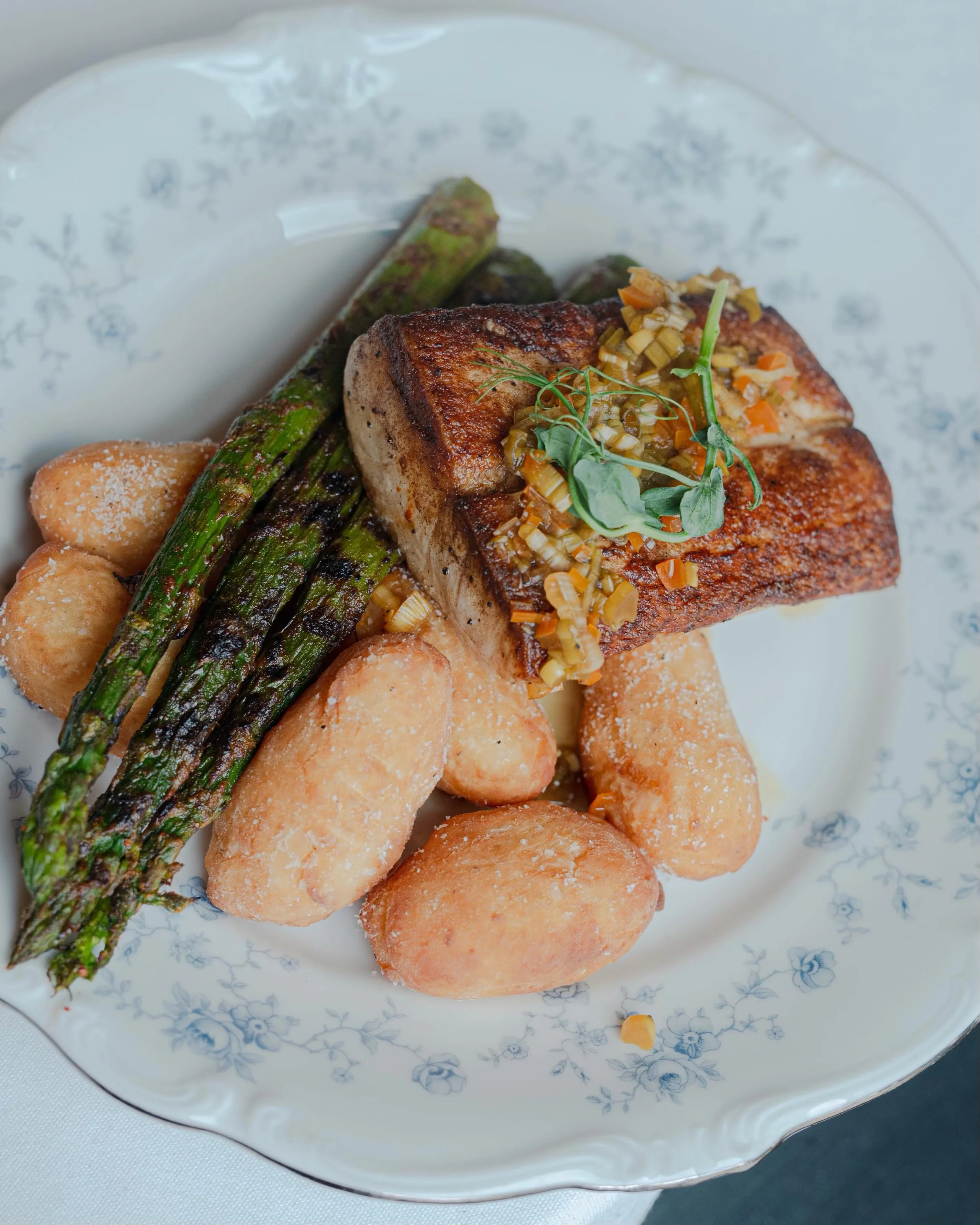 Tired of the gray? ☁️ Our summer menu is brining all the warm, sunny vibes! 

Pictured here:
🌶️ Mahi Mahi drizzled with green onion &amp; aji relish,  parmesan yuca tots and grilled asparagus 
 🌽 Summer Scallops with Peruvian choclo and torched bab