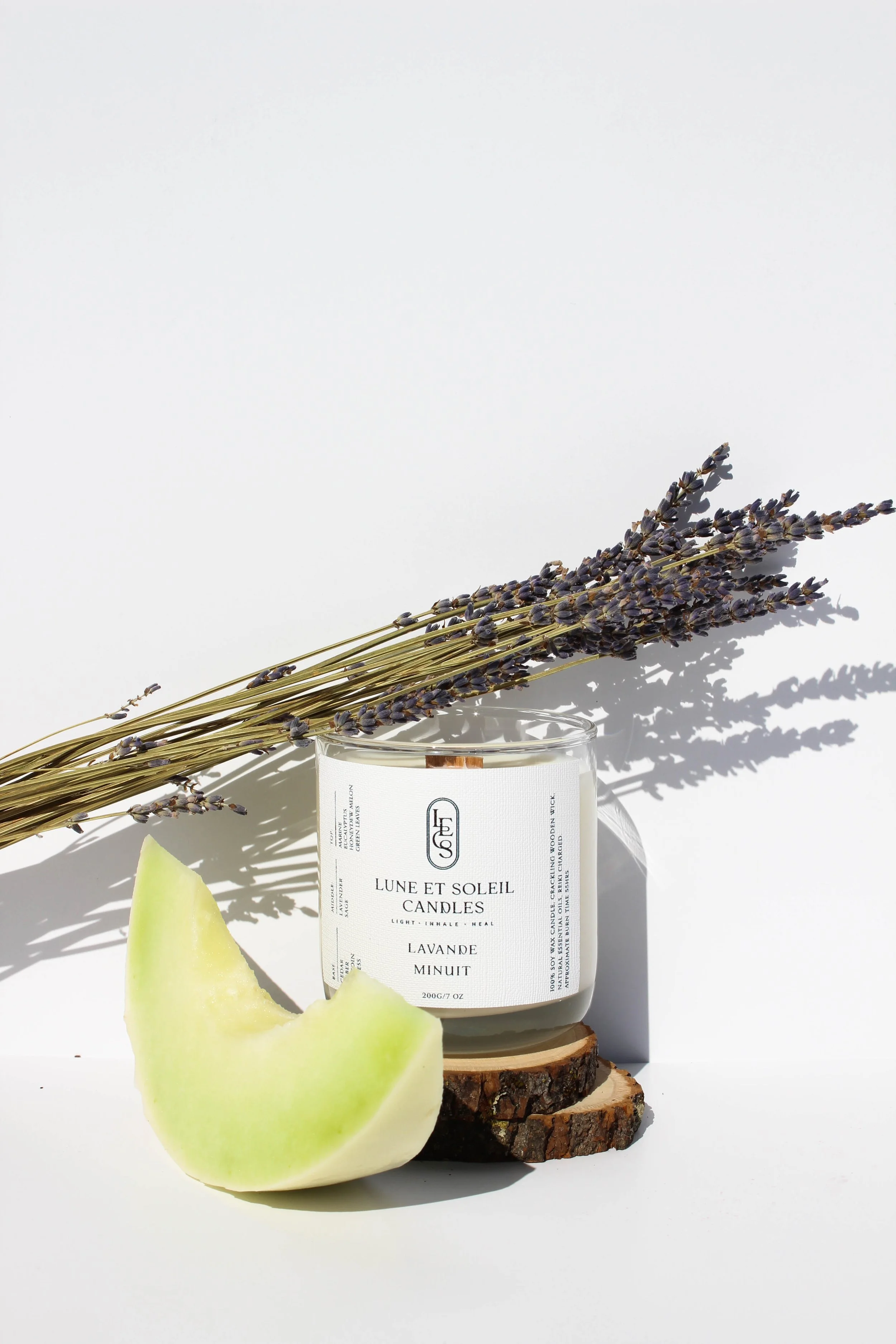 Lavande Minuit soy wax candle in a clear glass vessel styled with a melon wedge and lavender by Lune et Soleil