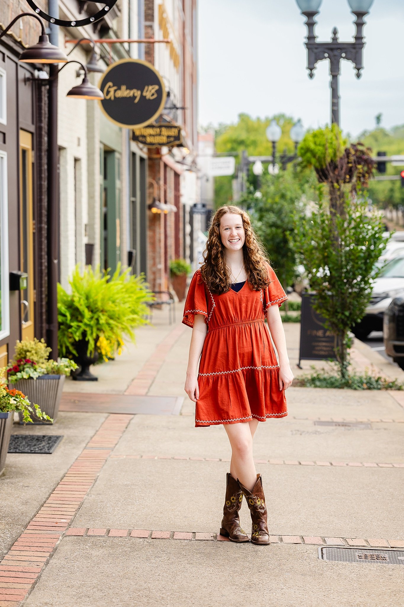 High school senior wearing a rust-colored dress and cowboy boots during a senior portrait session, showing an example of a well-planned outfit