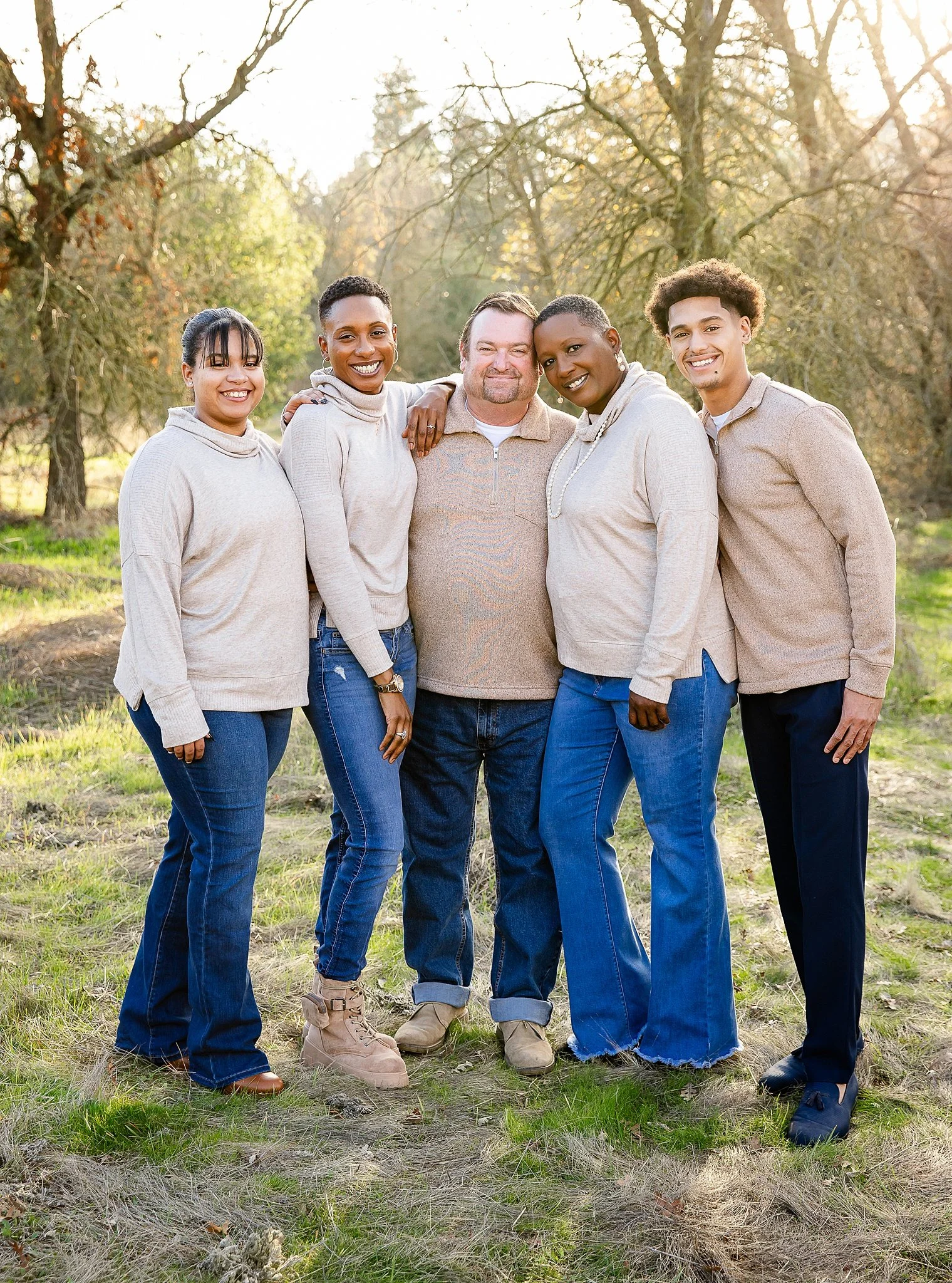 family of 5 wearing neutral colored tops and jeans outfits coordinating