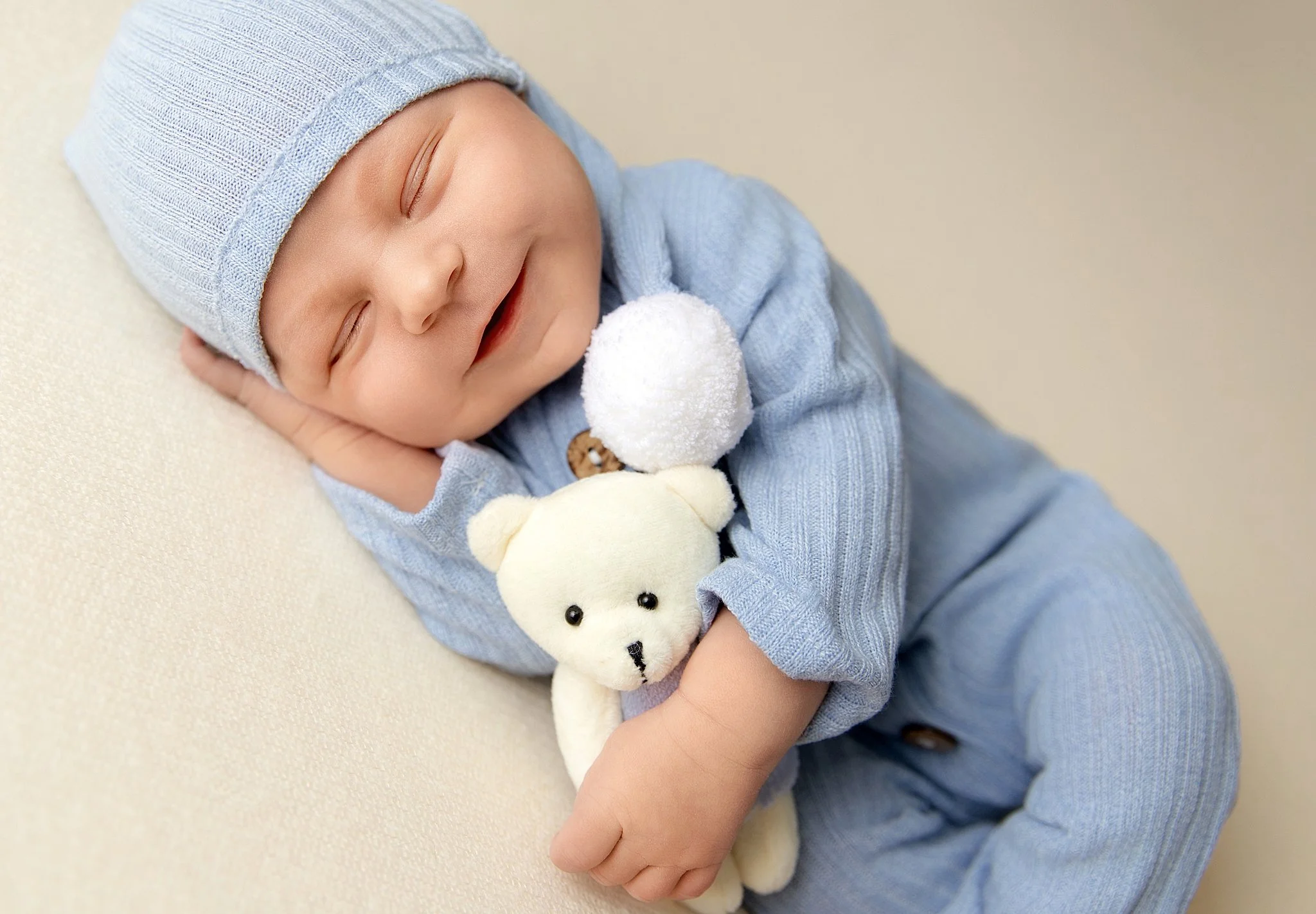 Sleeping newborn baby boy in a soft blue knit outfit cuddling a teddy bear during a studio session in Elk Grove, CA.