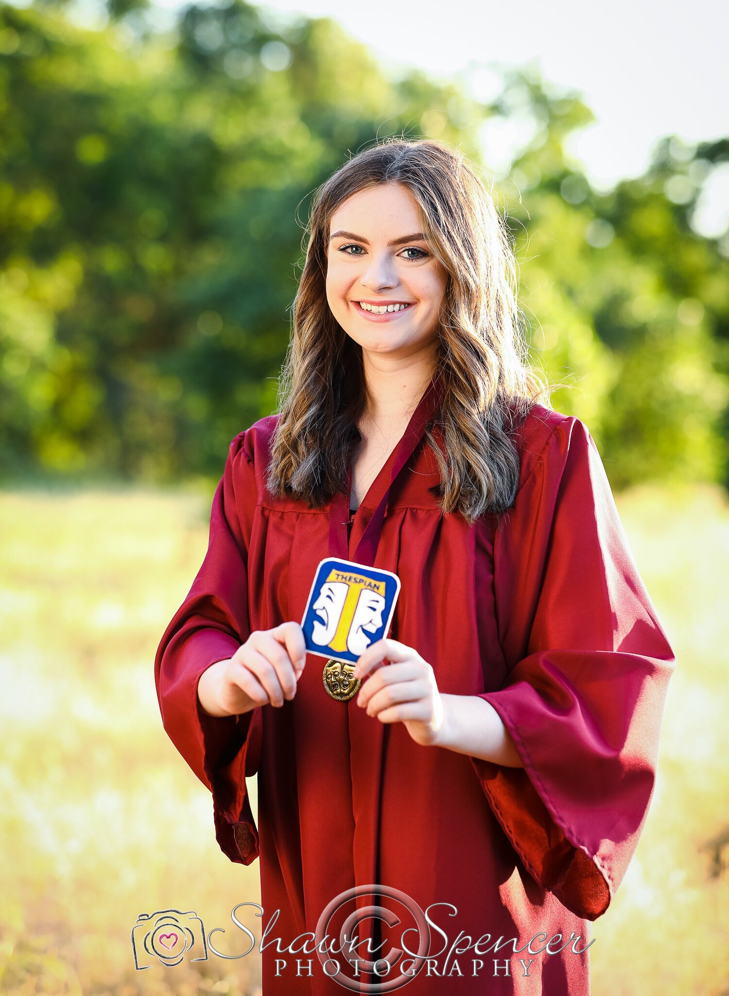  senior girl wearing graduation gown holding drama patch 