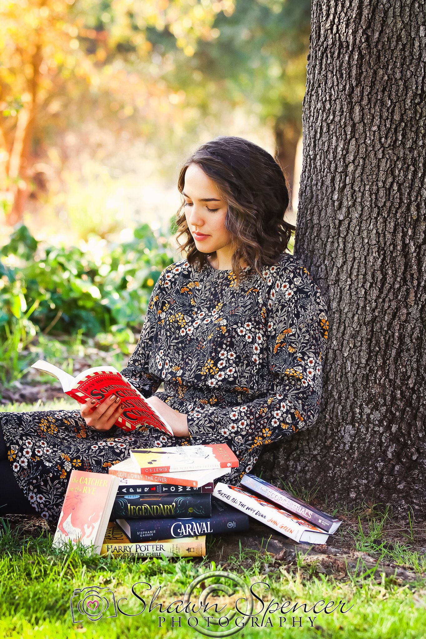  senior girl leaning against tree reading books 