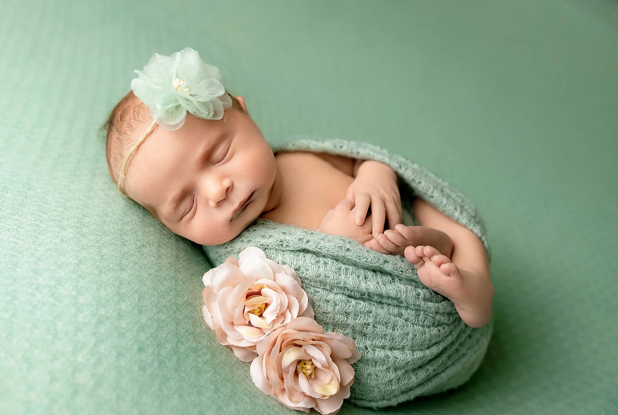 baby girl in green wrap with legs and hands showing on green beanbag layer with pink flowers