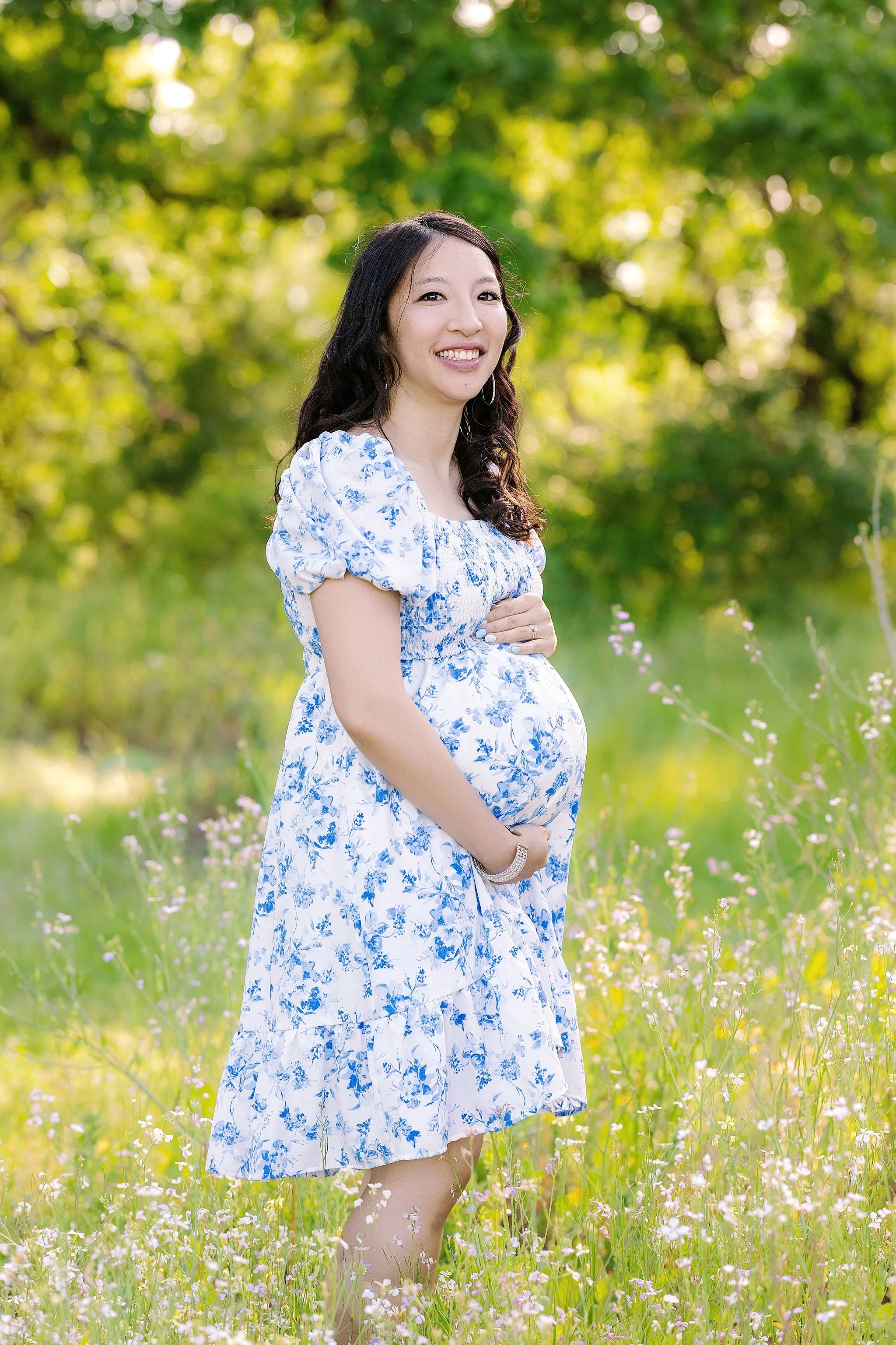 Outdoor maternity portrait of an expecting mother in a blue floral dress standing in a wildflower field during a session in Elk Grove, California