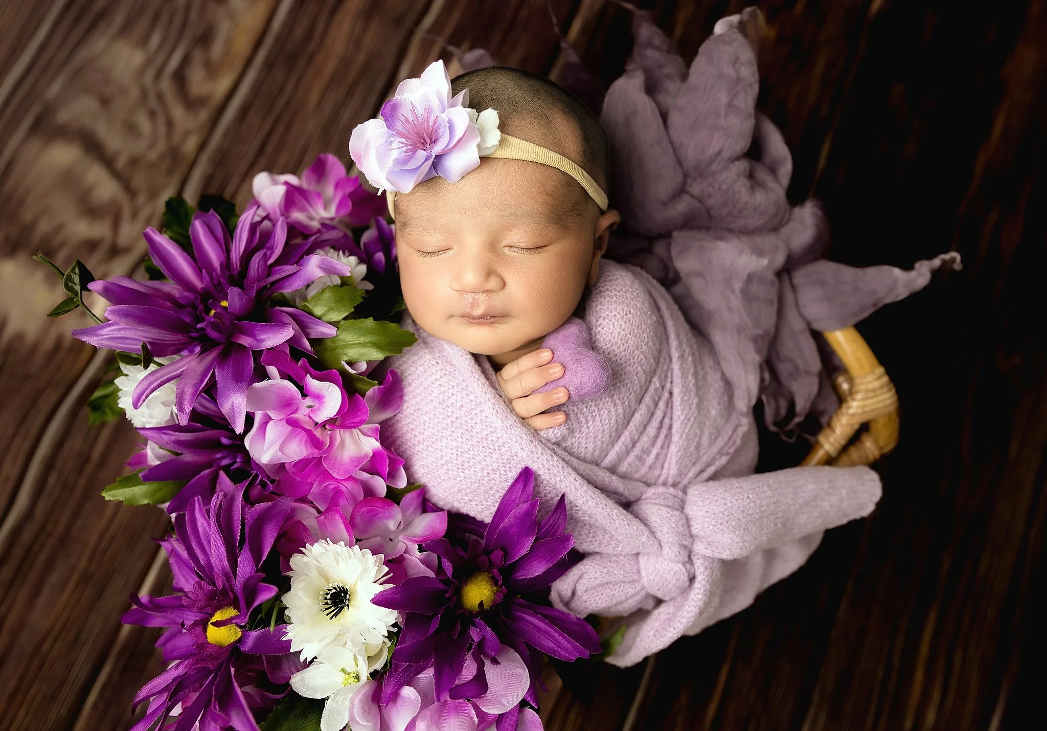 Newborn baby girl wrapped in lavender fabric posed in a basket with vibrant purple flowers during an Elk Grove newborn photography session.