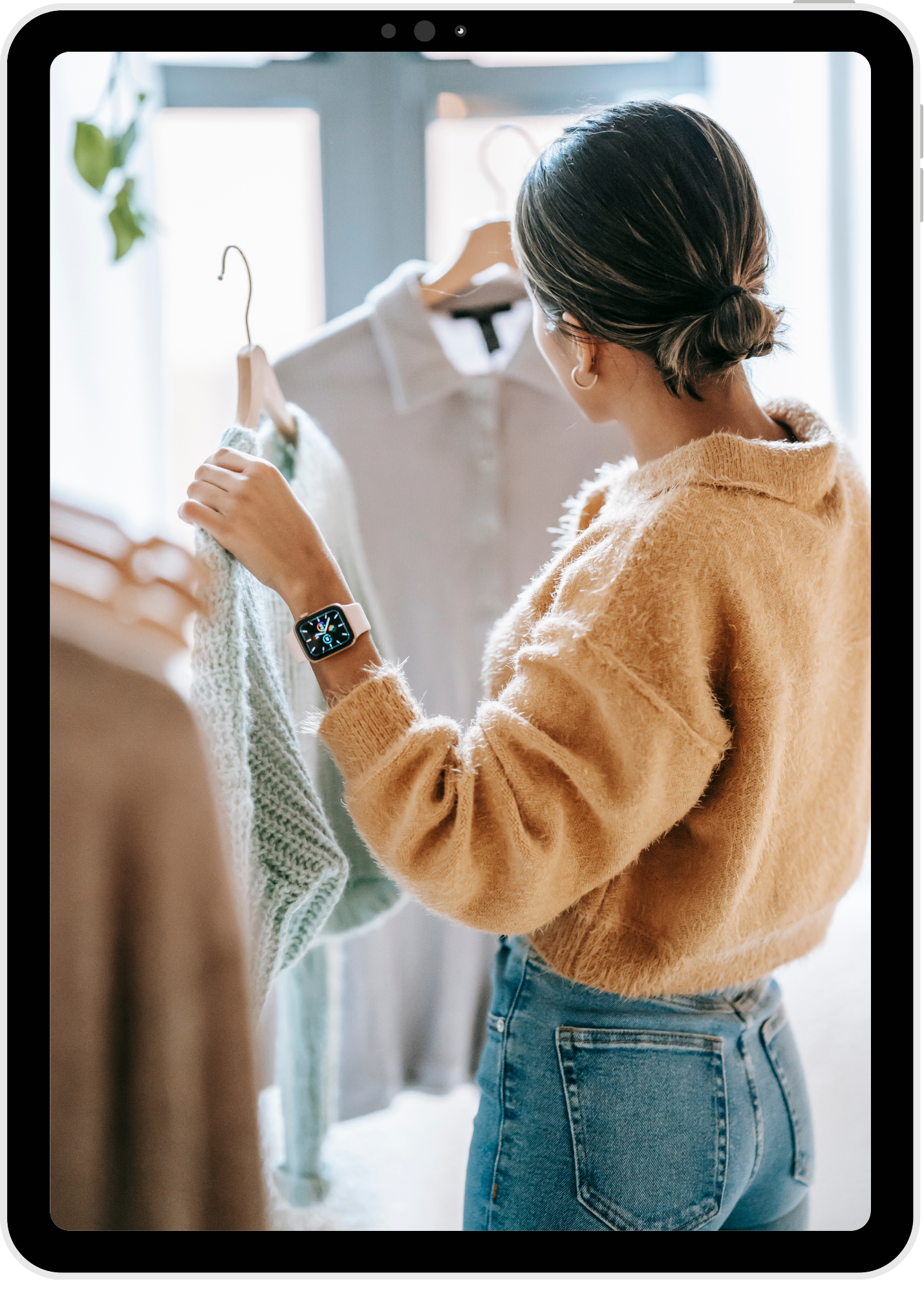 A senior girl choosing outfits on hangers in natural light, representing planning looks for a senior portrait session.