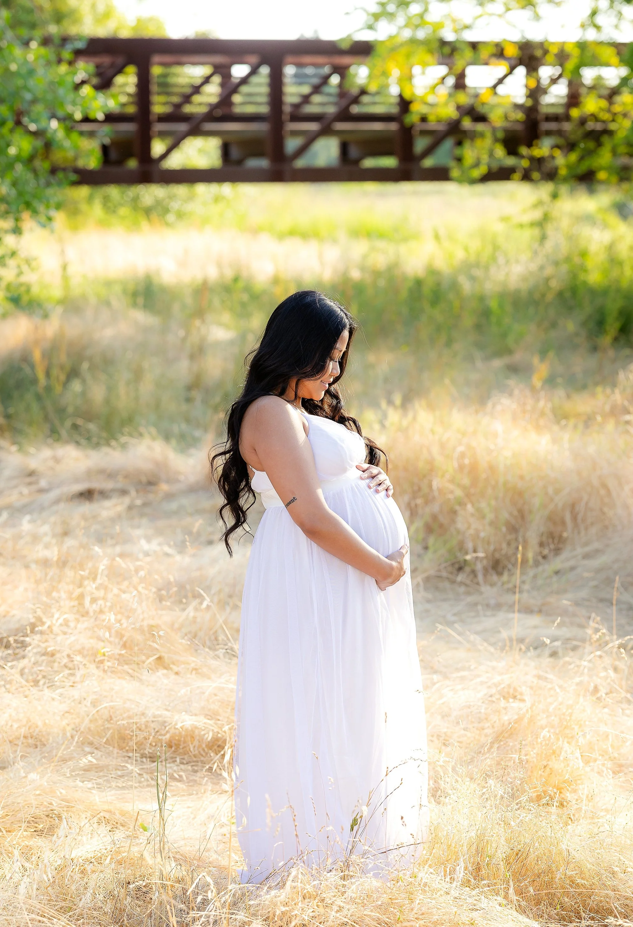 Expecting mother gently holding her baby bump during an outdoor maternity photo session in a sunlit field in Elk Grove, California