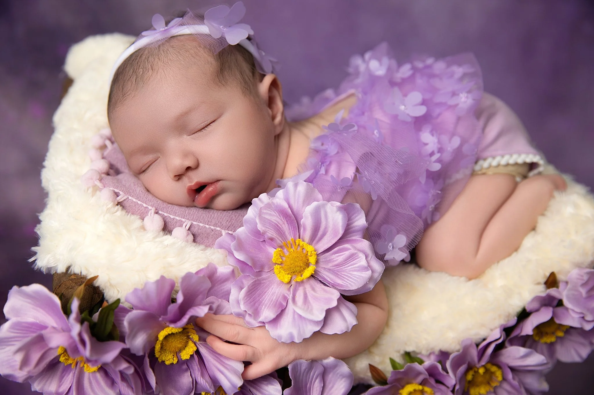 Newborn baby girl in a soft purple outfit surrounded by lavender flowers during a studio session in Elk Grove, CA.