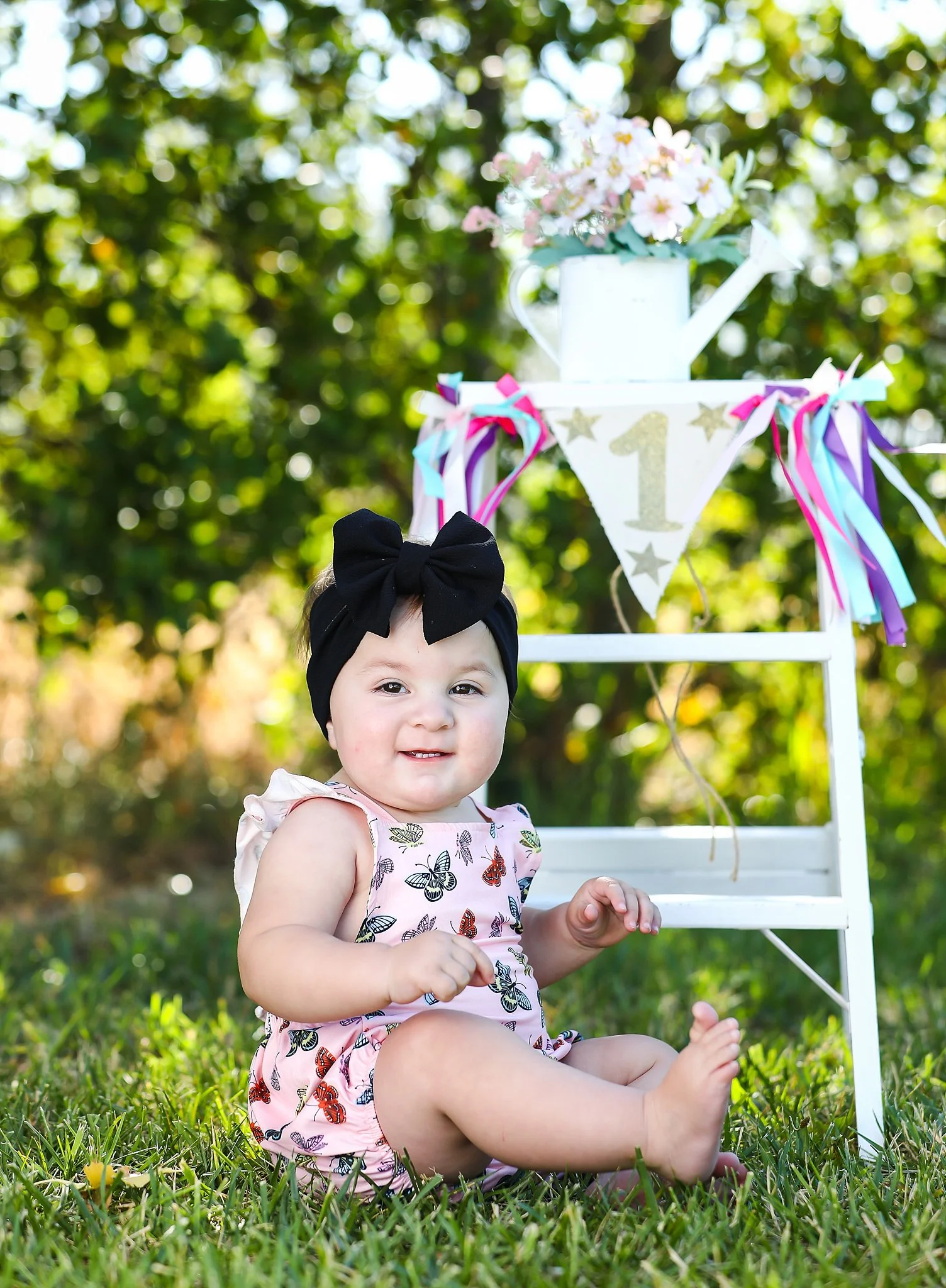 One-year milestone portrait of baby girl sitting outdoors with floral decor and first birthday banner in Elk Grove, California.
