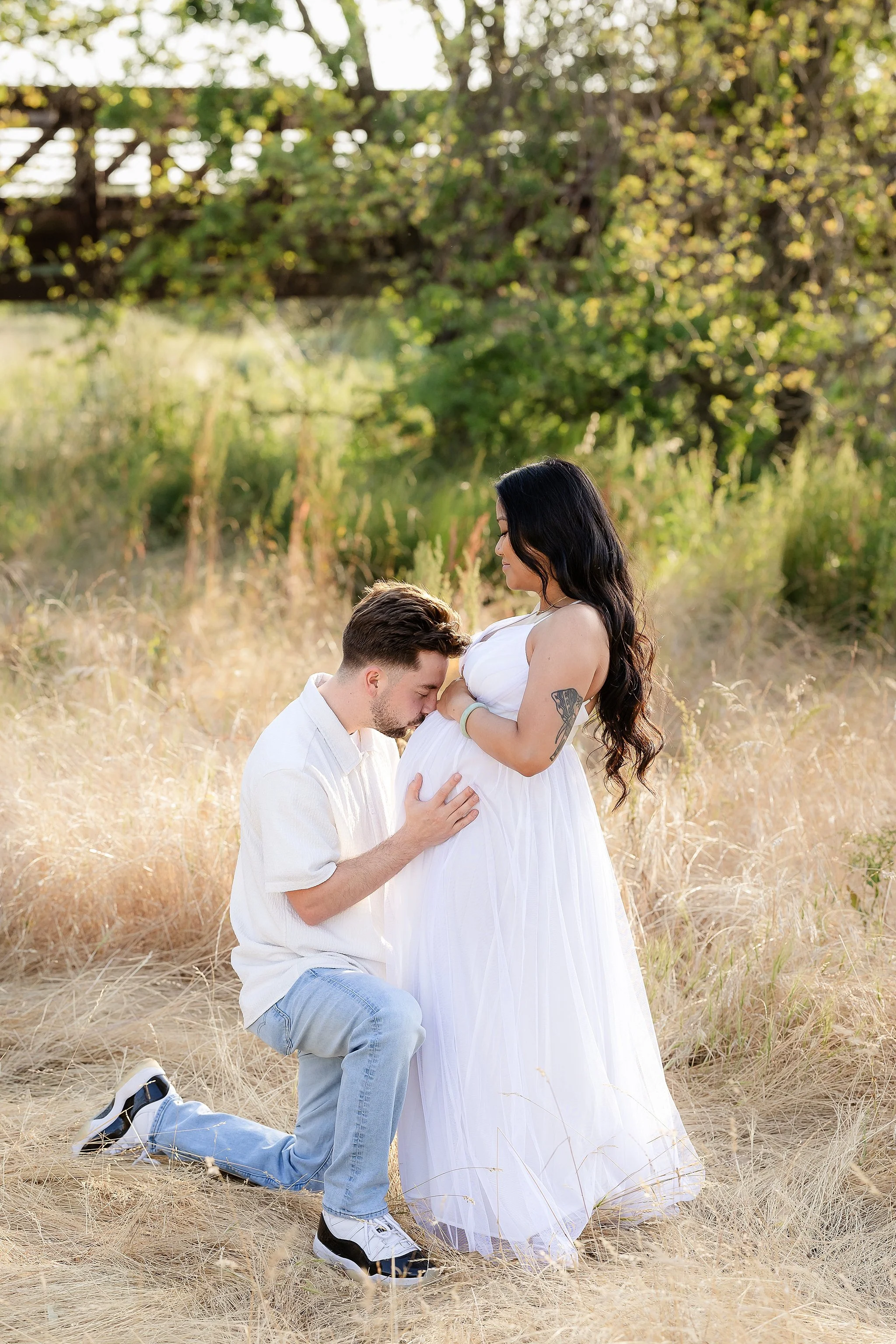 Expecting couple during an outdoor maternity session, with dad kneeling and kissing mom’s baby bump in Elk Grove, California