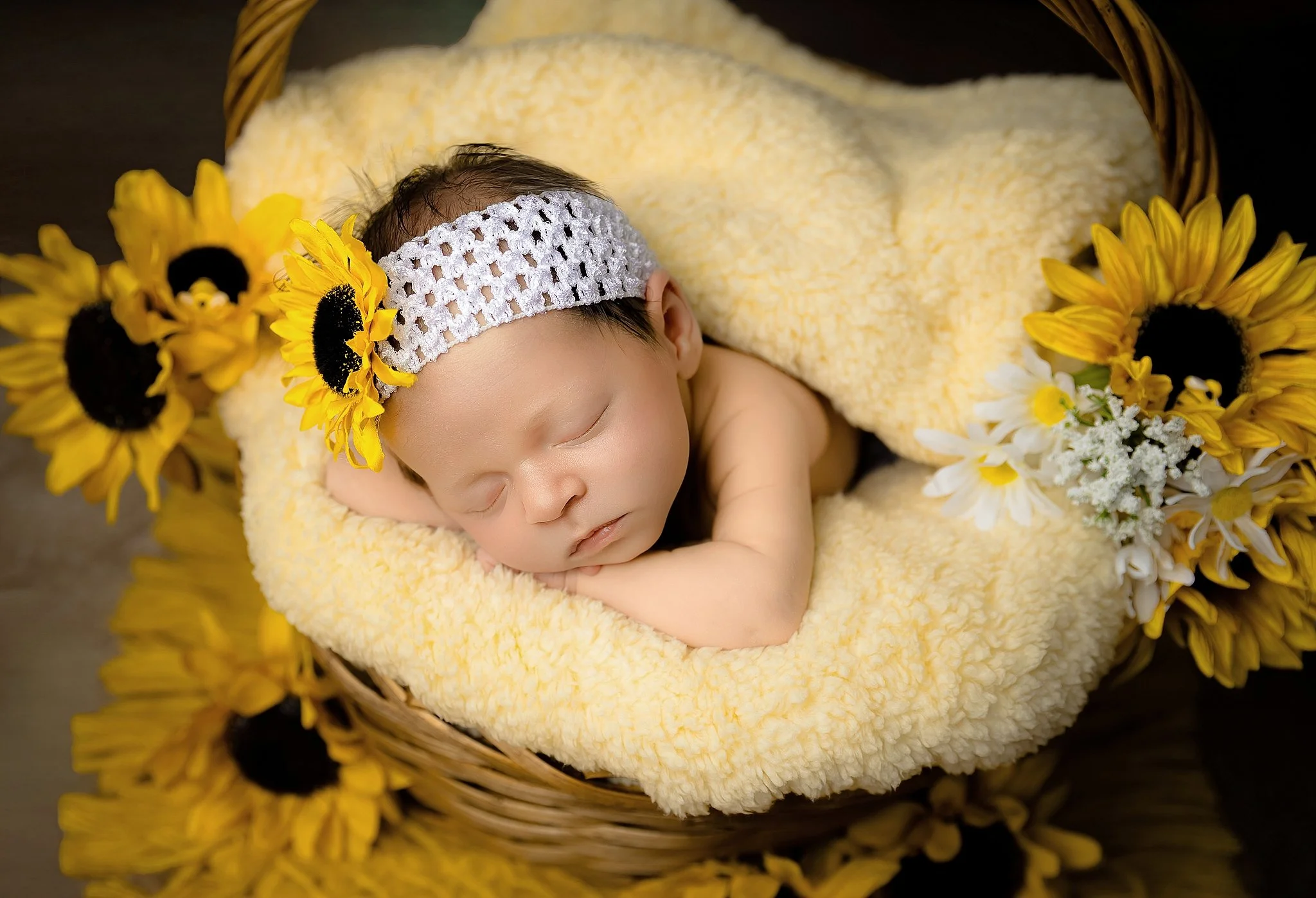 Sleeping newborn baby girl in a wicker basket surrounded by bright yellow sunflowers during a studio session in Elk Grove, California.
