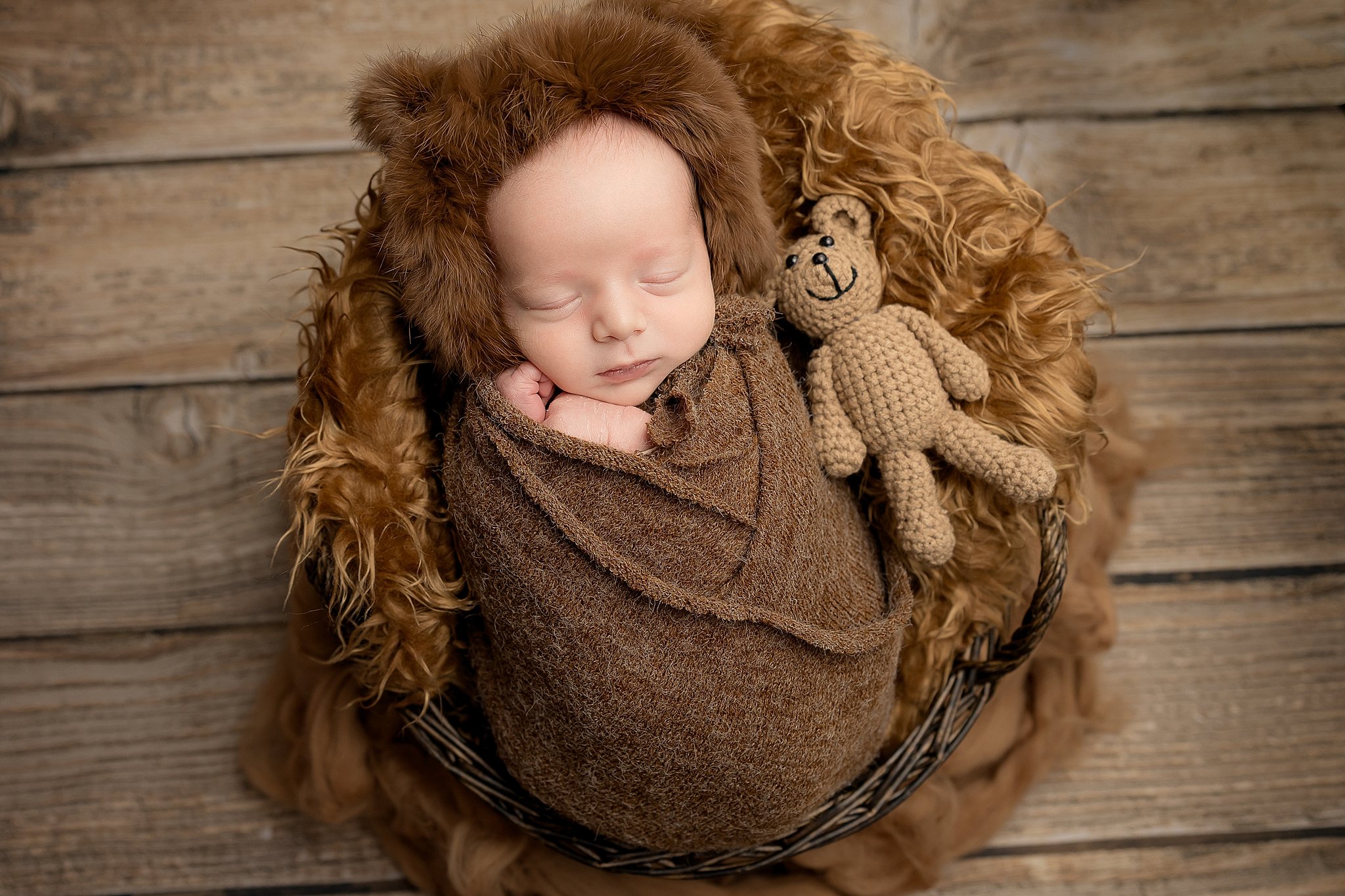 Newborn baby wrapped in a soft brown wrap and bonnet sleeping in a basket during a studio session in Elk Grove, California.
