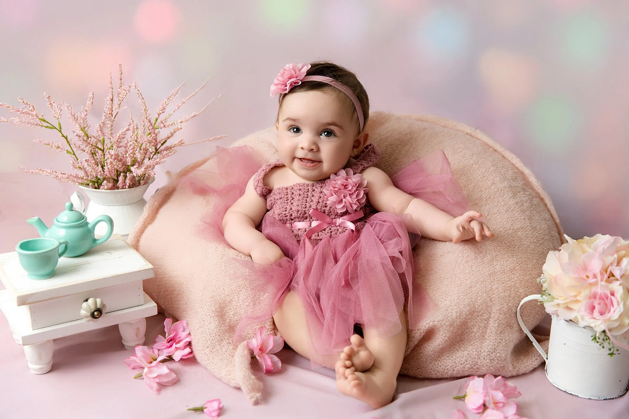 Six-month-old baby girl smiling while sitting on a soft pink chair during a studio milestone photography session in Elk Grove, California.