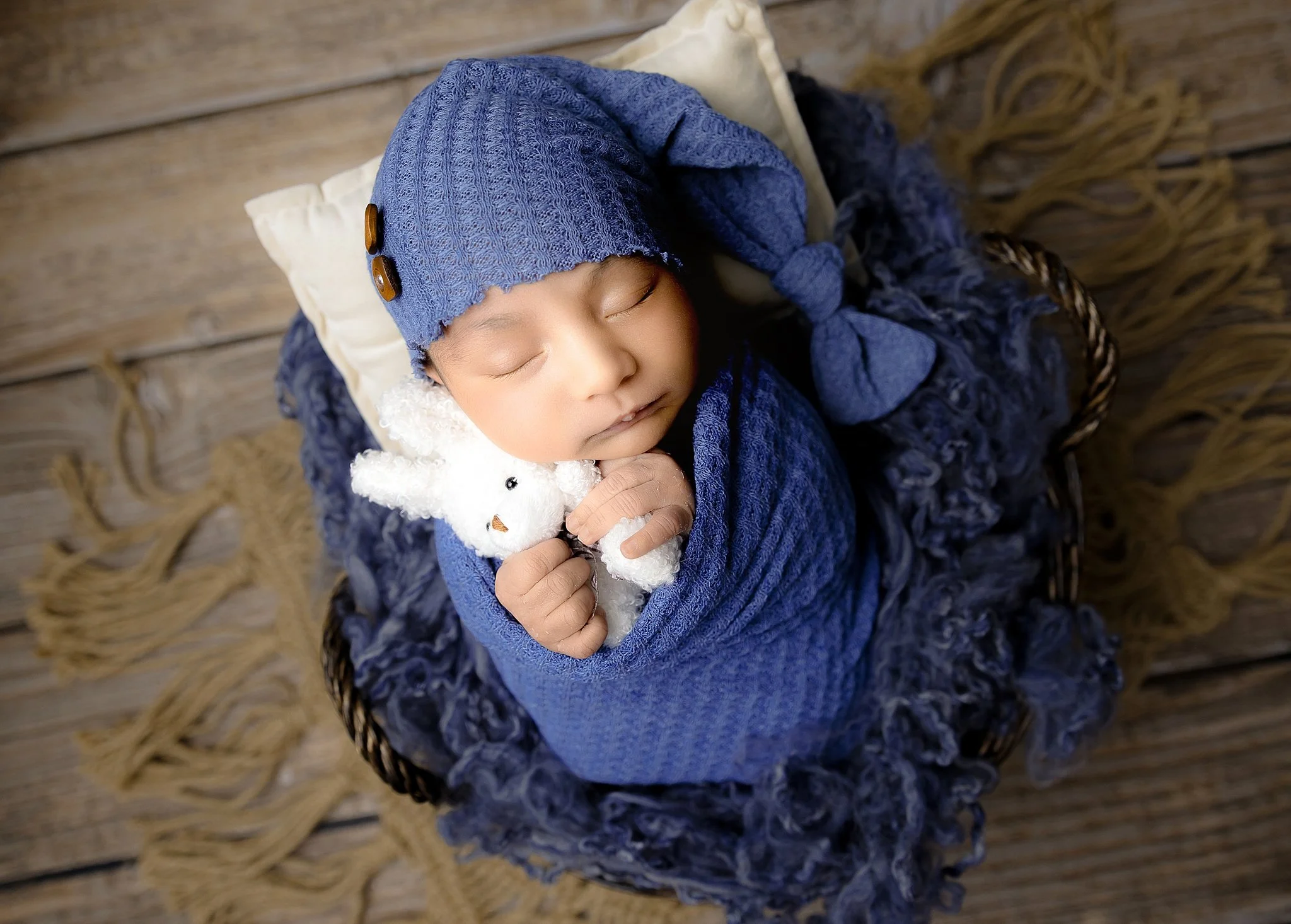 Newborn baby wrapped in deep blue fabric and bonnet holding a small stuffed bunny during a studio session in Elk Grove, CA.