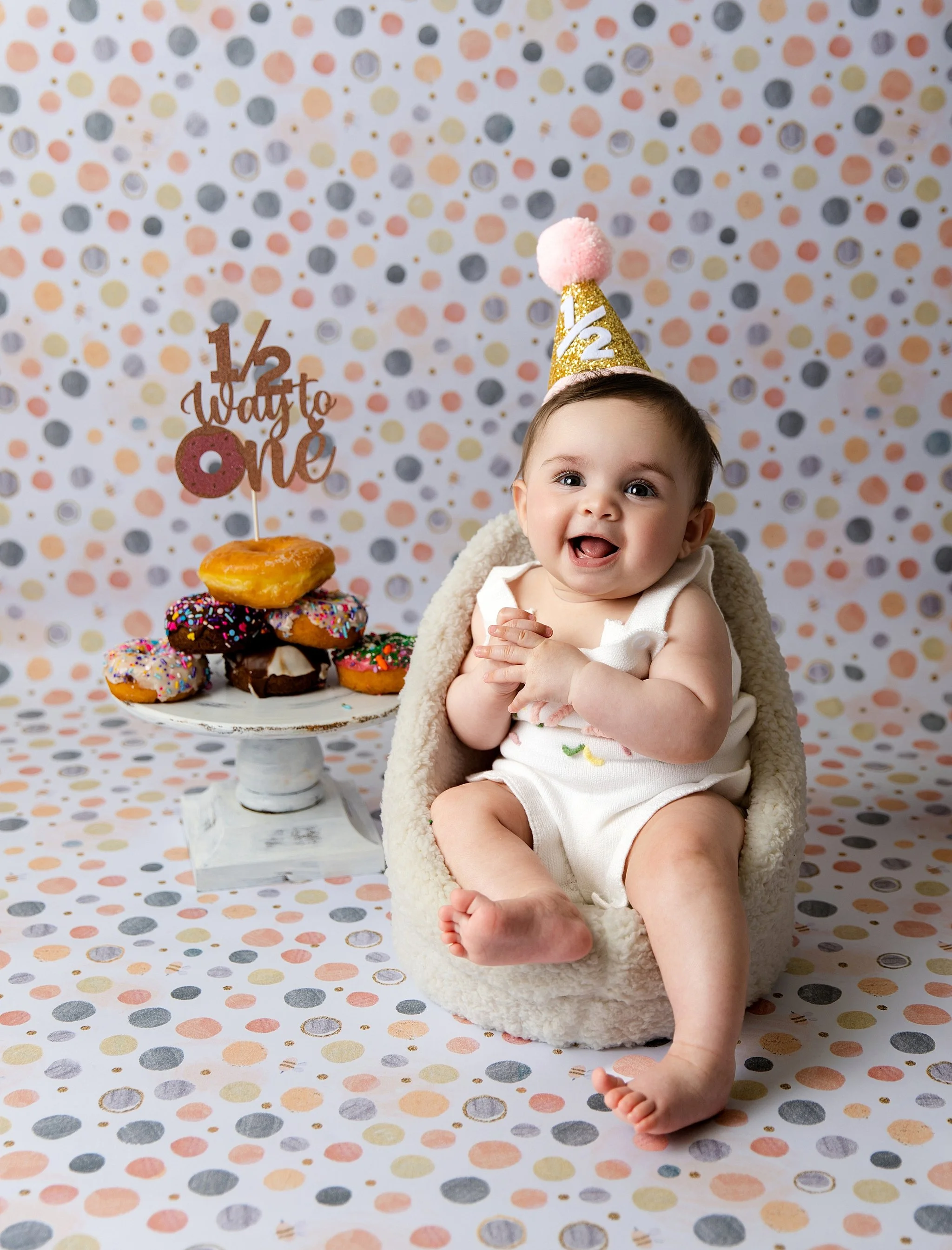 Happy six-month-old baby girl celebrating her half birthday with donuts during a studio milestone photography session in Elk Grove, California.