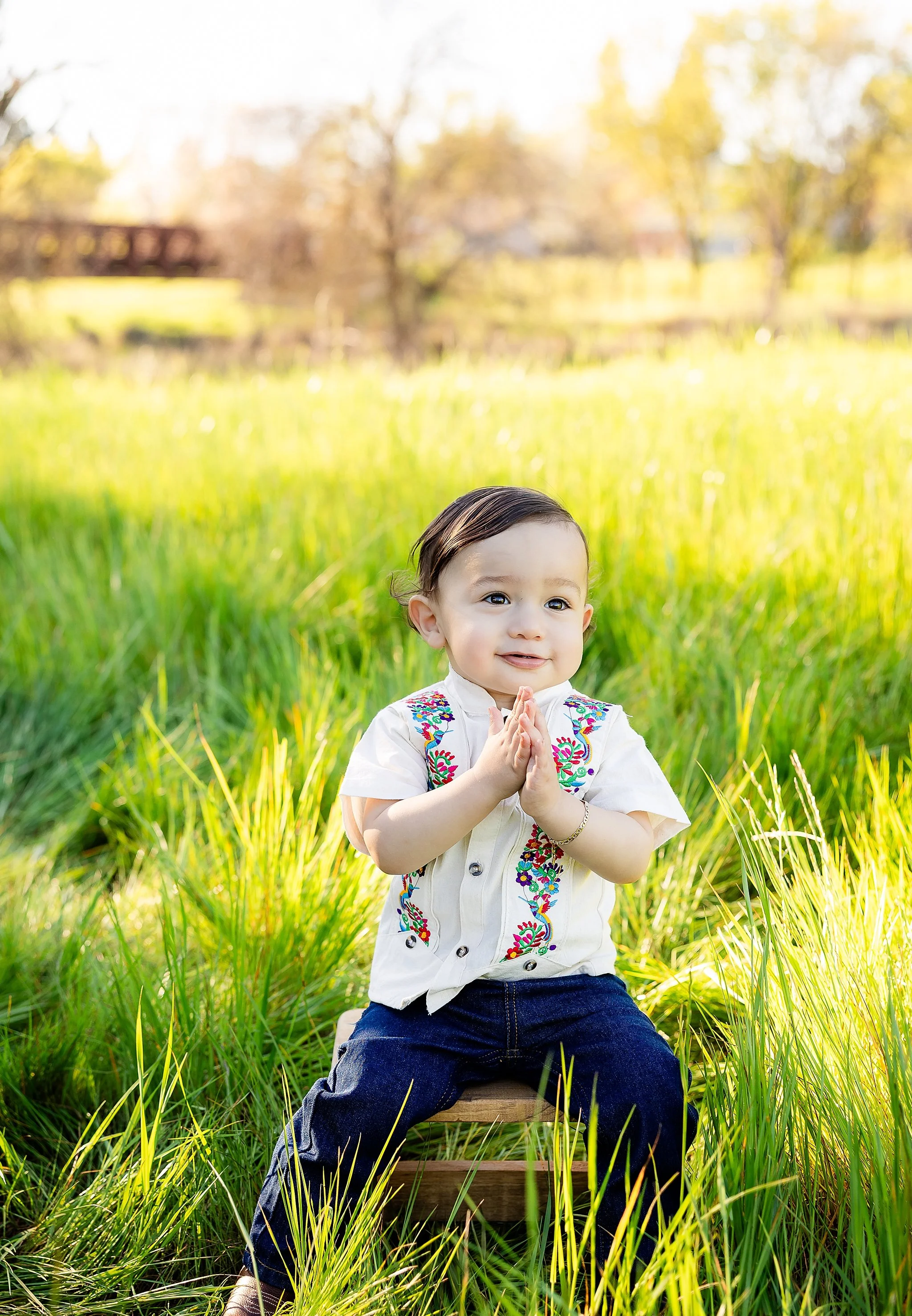 One-year-old boy smiling while sitting in a grassy field during an outdoor milestone portrait session in Elk Grove, California.