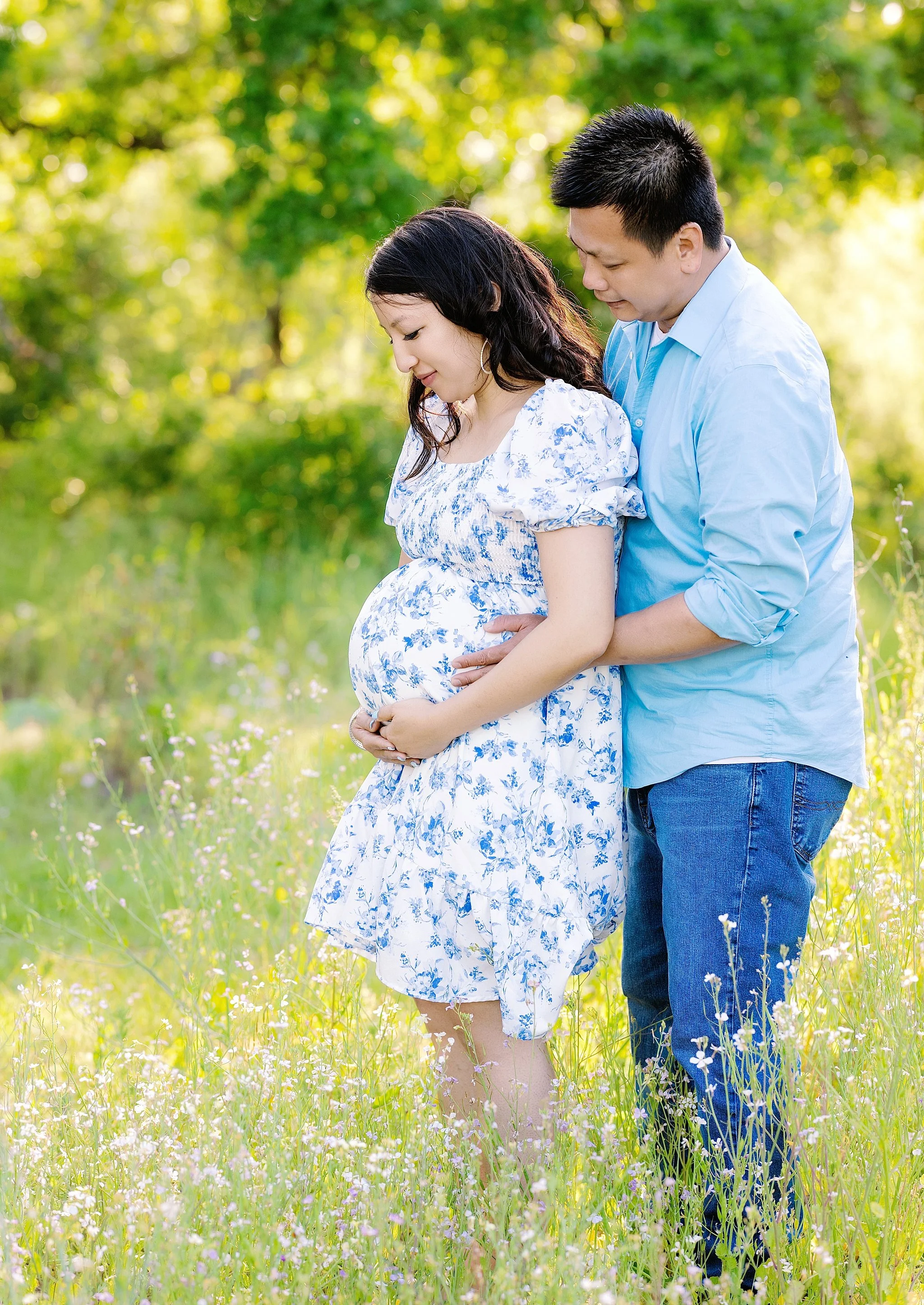 Expecting mother in a blue floral dress with her partner embracing her from behind in a wildflower field during a maternity session in Elk Grove, California