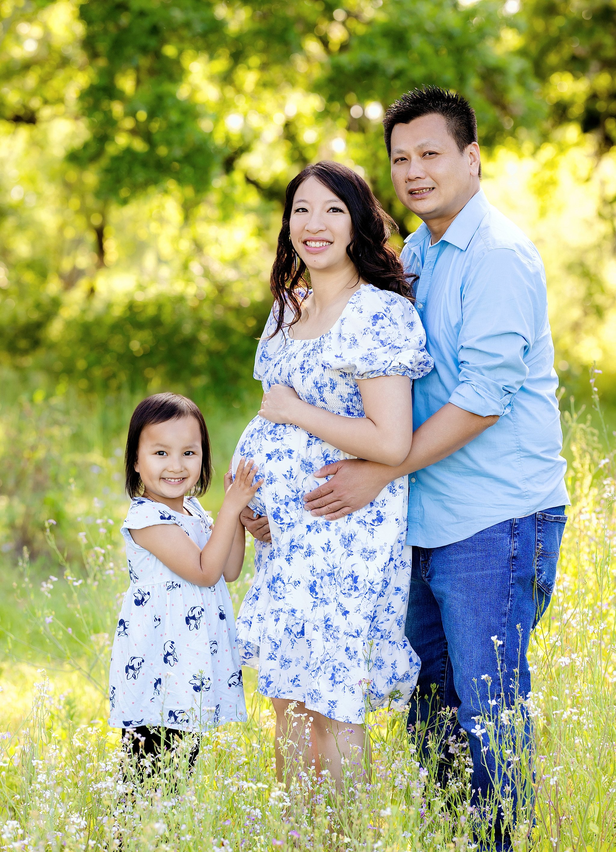 Maternity family portrait of expecting parents and their young daughter standing together in a wildflower field during a golden hour session in Elk Grove, California