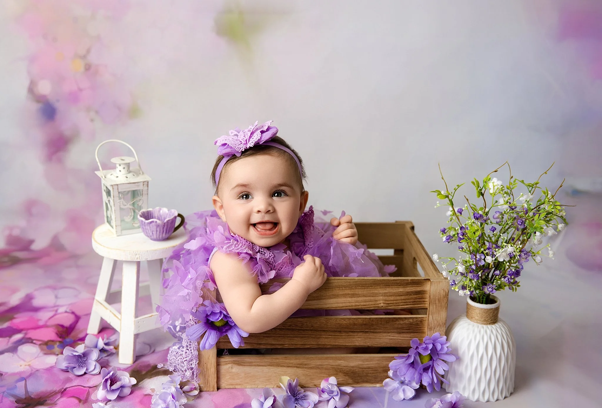 Six-month milestone portrait of baby girl in a purple outfit sitting in a wooden crate with floral accents photographed in Elk Grove, California.