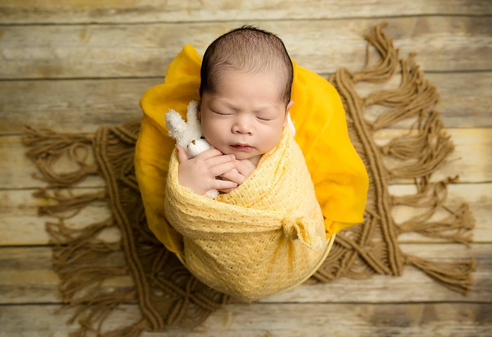 Newborn baby wrapped in a soft yellow blanket holding a small stuffed bunny, posed in a basket during a studio session in Elk Grove, California.