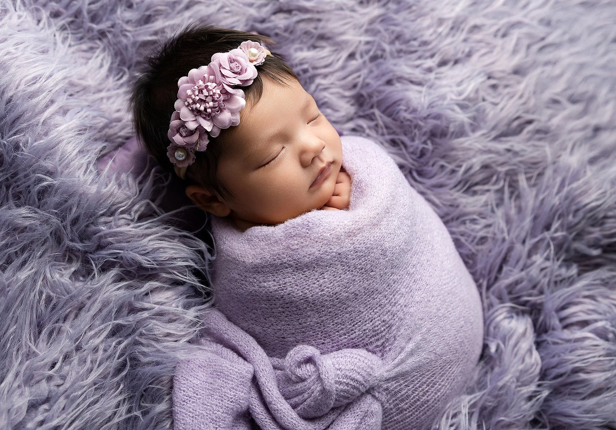 Sleeping newborn baby girl wrapped in soft lavender fabric on a textured fur backdrop in an Elk Grove newborn studio.