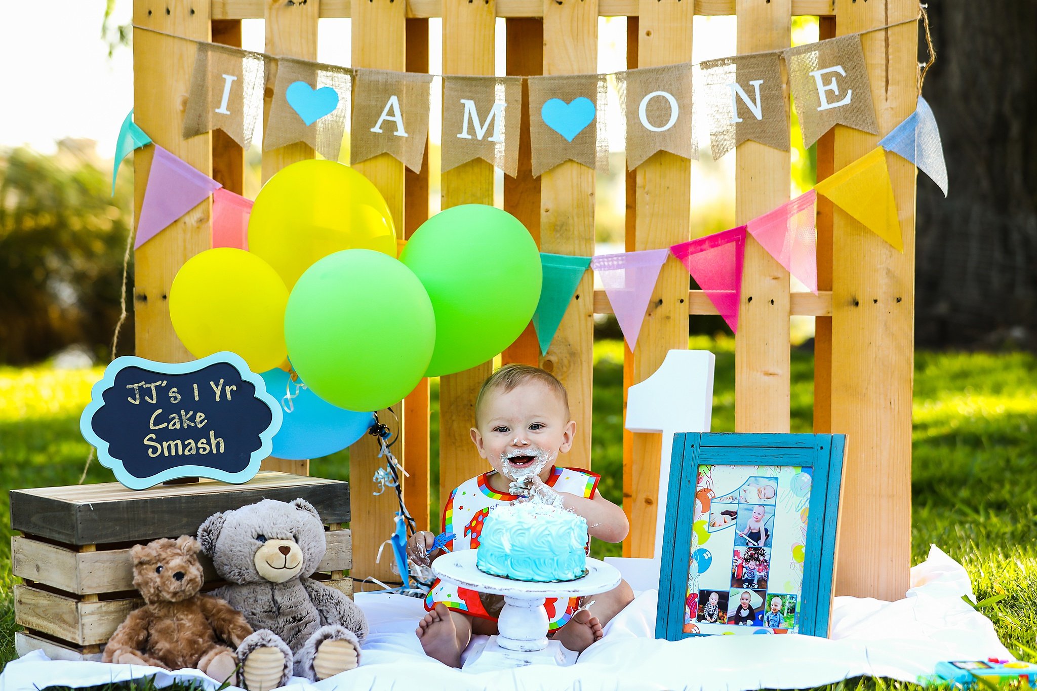 First birthday cake smash session with baby boy and blue cake surrounded by balloons and wooden backdrop in Elk Grove, CA.