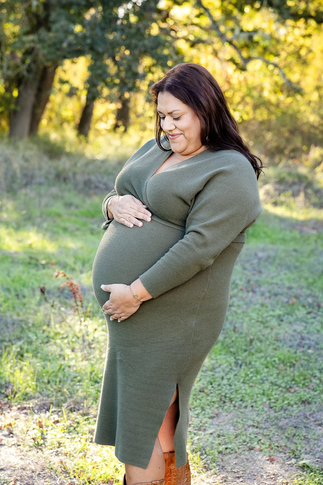Outdoor maternity portrait in Elk Grove, California of an expecting mother in a green dress looking down and holding her baby bump