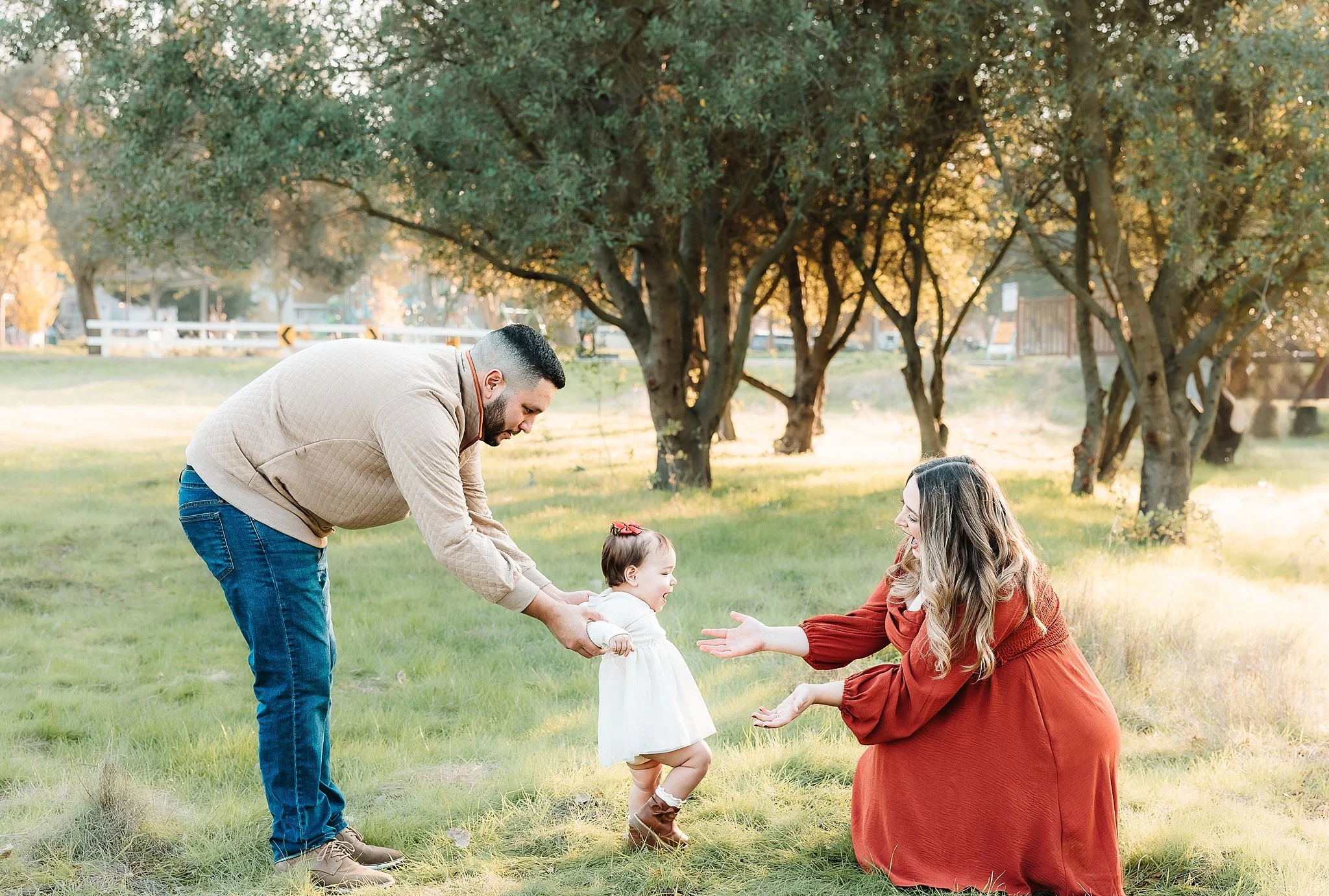 Mom and dad encouraging their young daughter as she walks between them during an outdoor family photo session in Elk Grove.