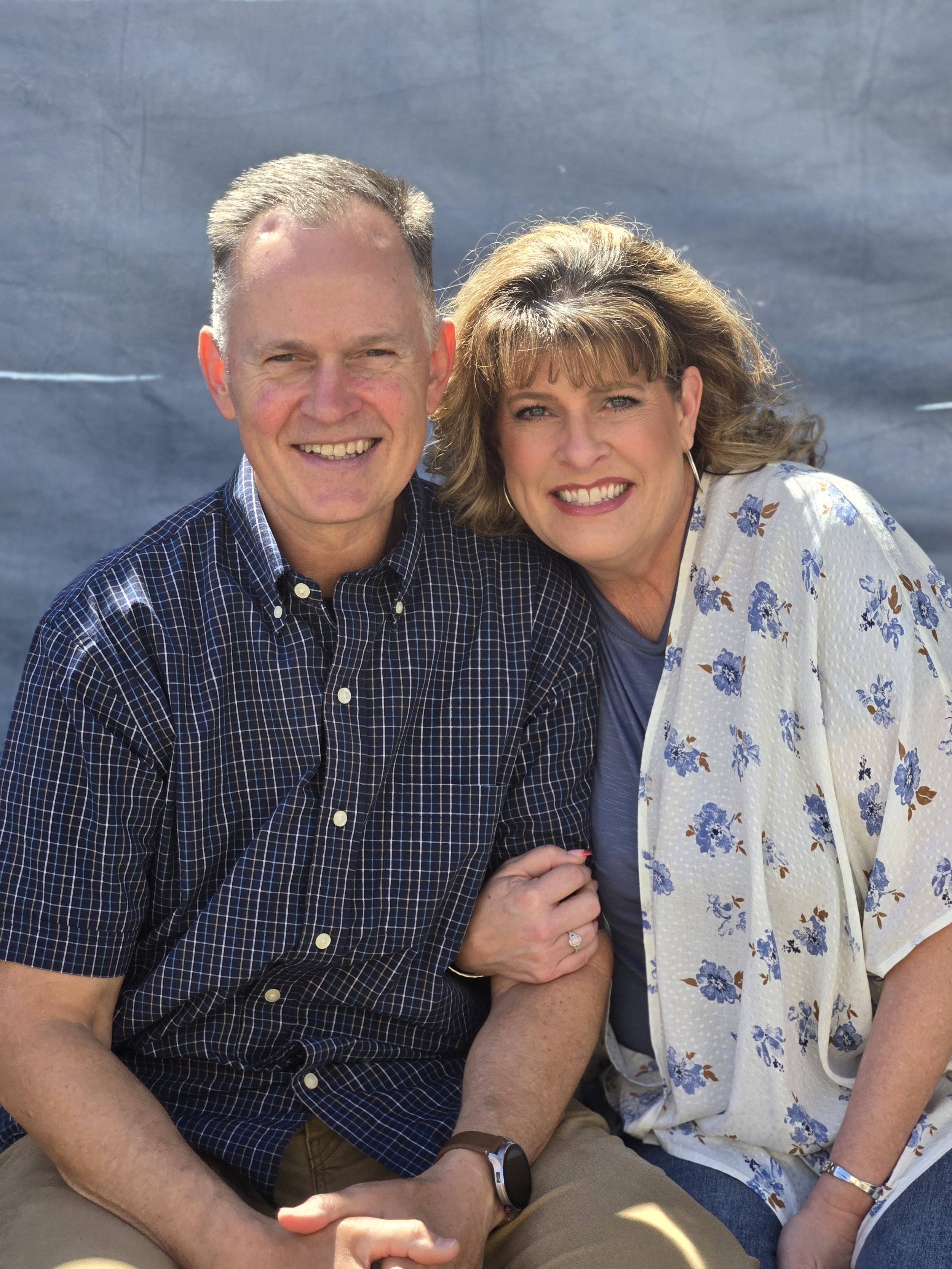 A husband and wife sitting close together with blue backdrop wearing light blue clothing.
