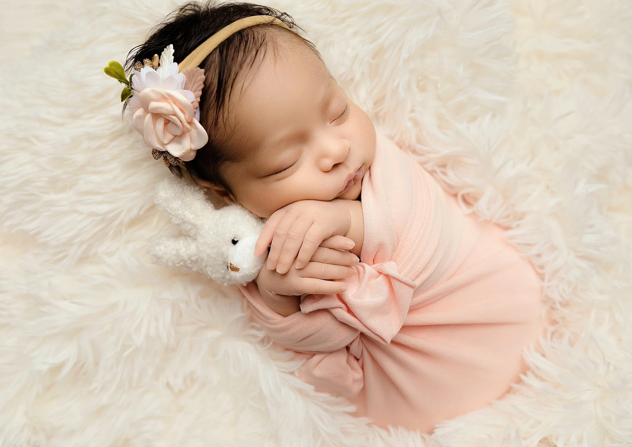 Sleeping newborn baby girl wrapped in blush fabric with a floral headband, photographed in a home studio in Elk Grove, California.