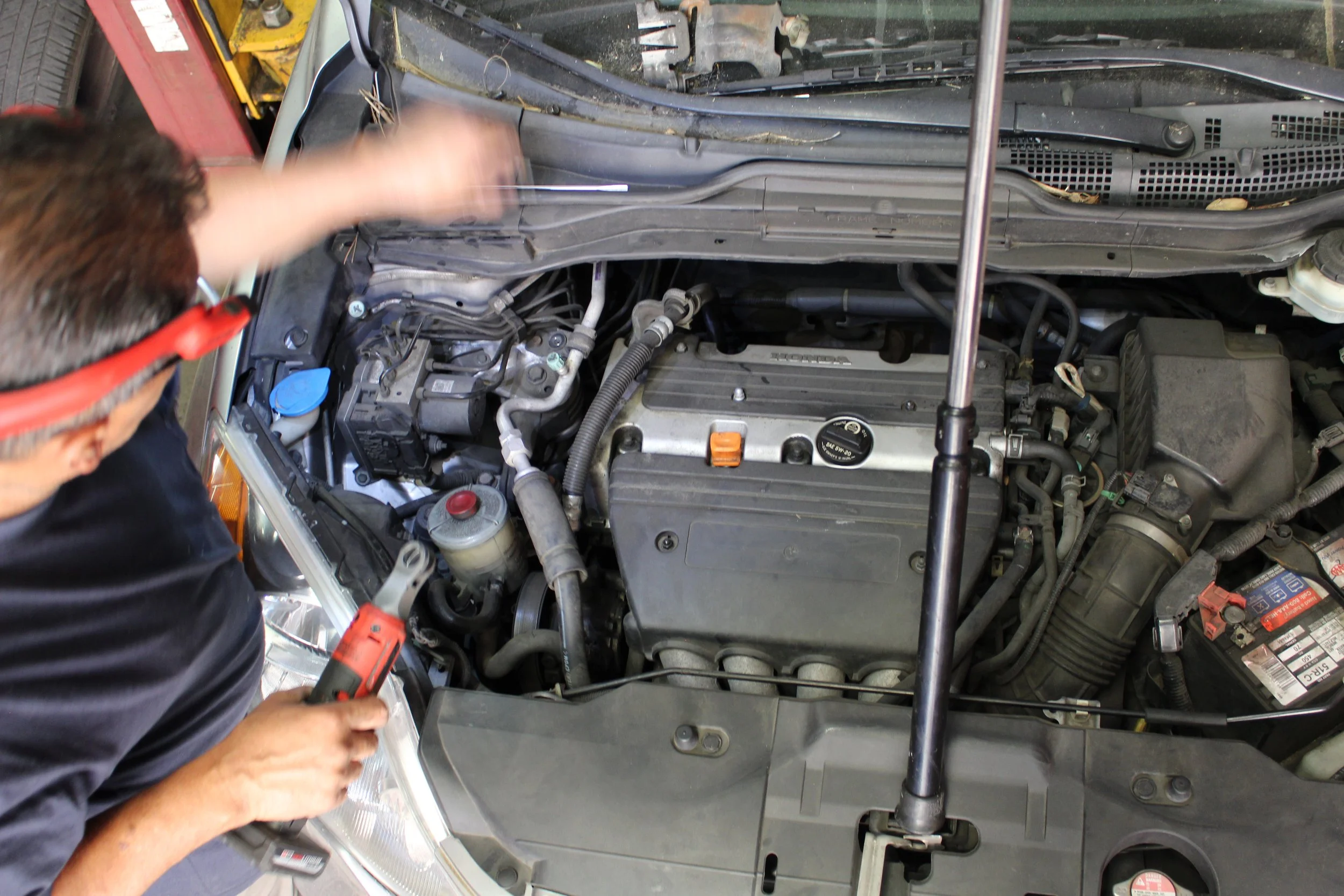 A mechanic working on a car engine, using tools in an auto repair shop.