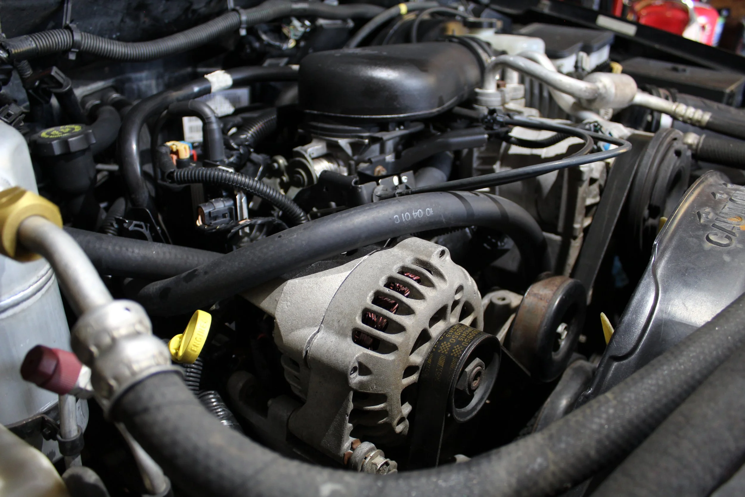 Close-up of a car engine showing a silver alternator, black belts, and various hoses and components.