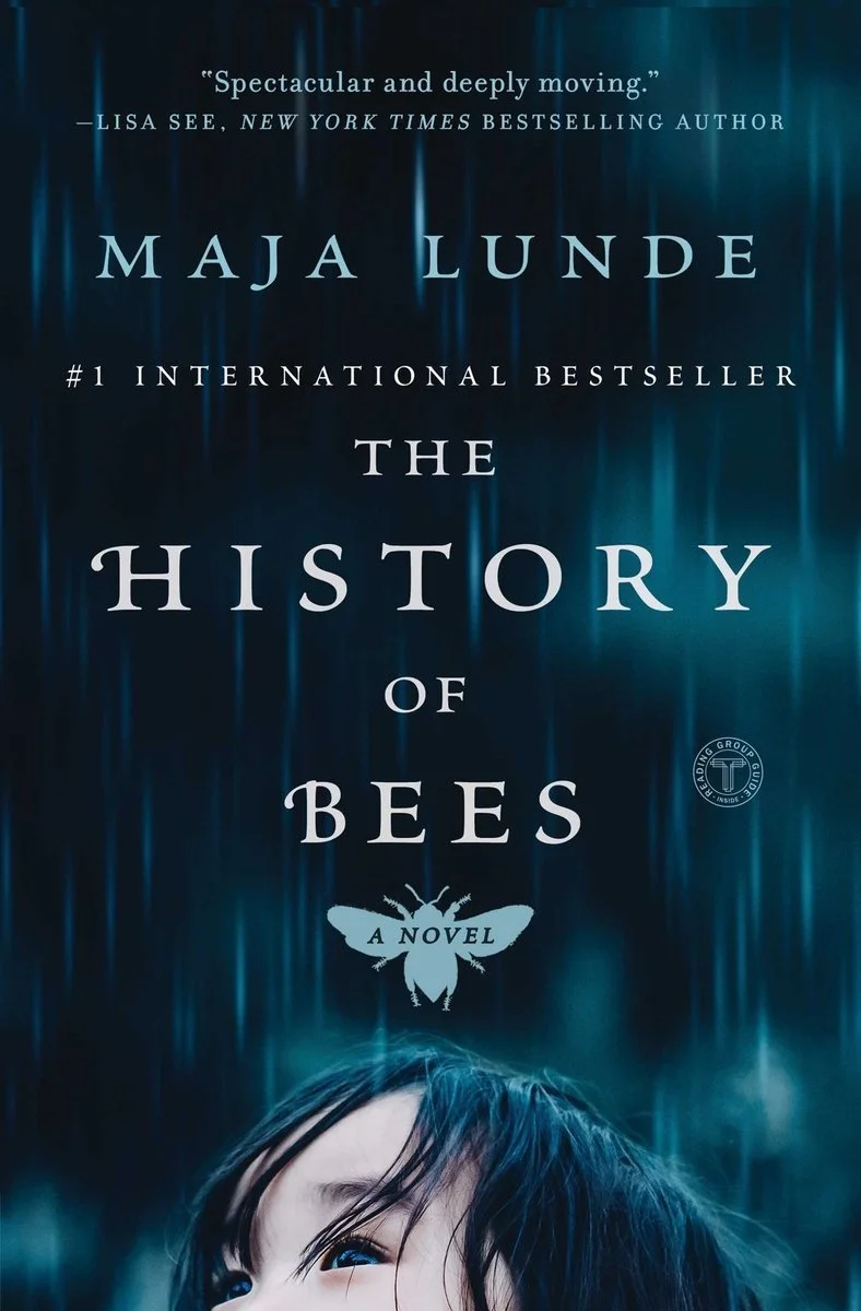 Book cover of 'The History of Bees' by Maja Lunde. The cover features a dark blue background with streaks of lighter blue and an image of a partial face of a person with dark hair at the bottom. The title and author's name are prominently displayed.