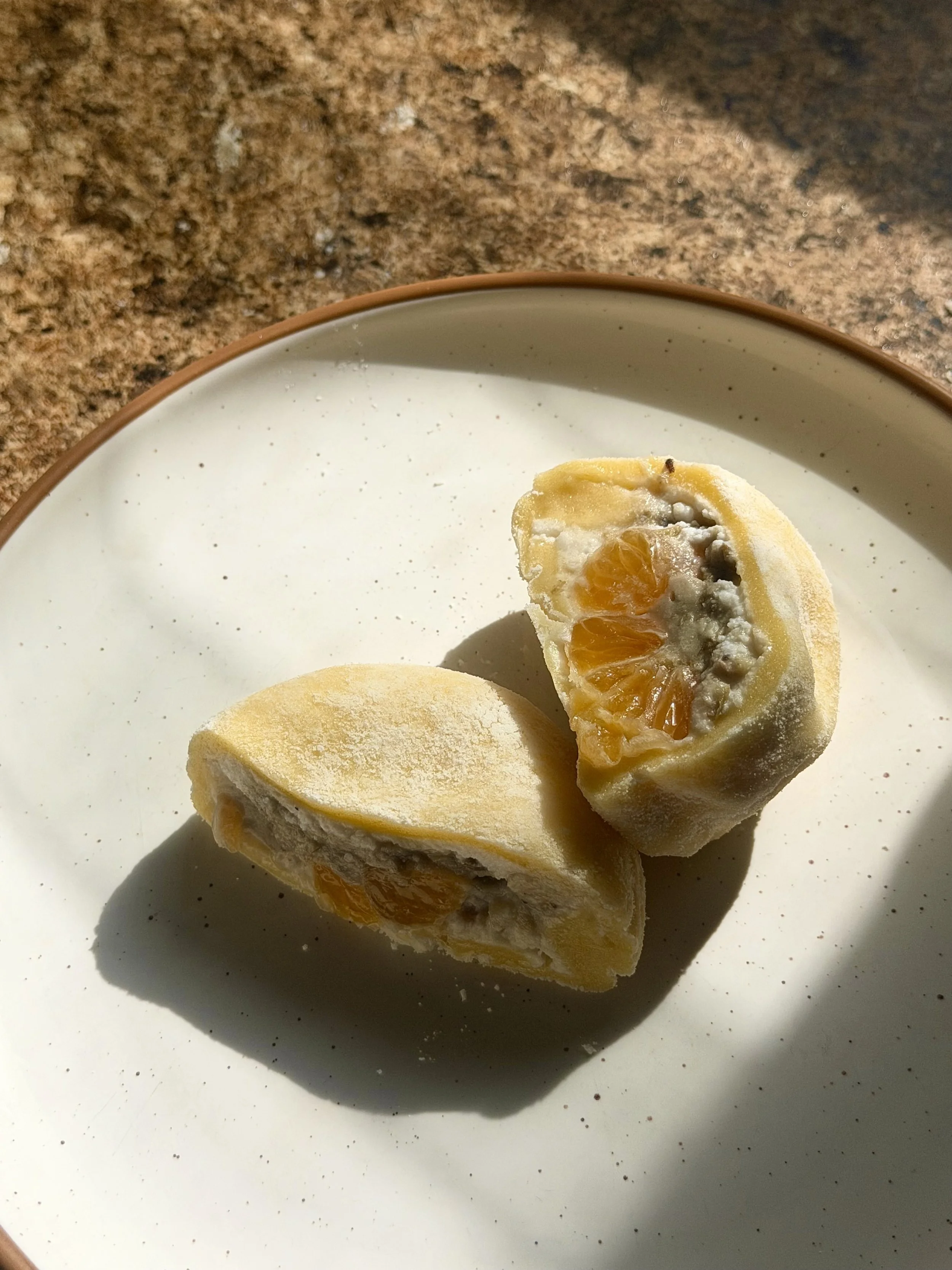 Homemade Korean tangerine mochi cut in half, naturally orange from fresh unpasteurized Jeju tangerine juice, filled with whipped coconut cream, fresh tangerine, and honey-sweetened mungbeans for gut and skin health.