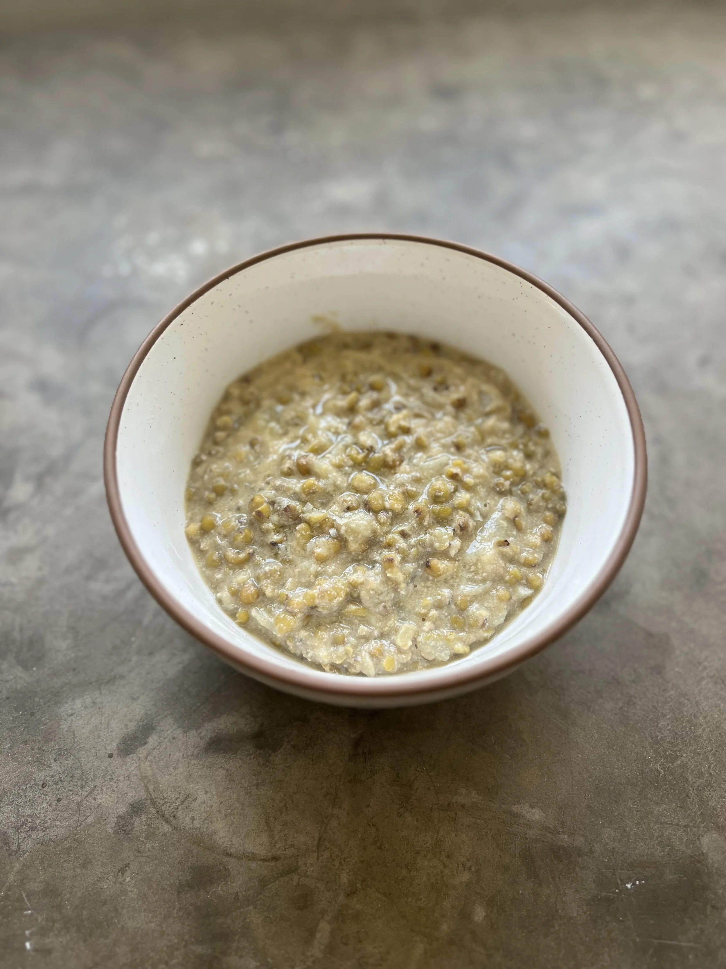 Steamy bowl of coconut mungbean stew made with bone broth, ginger, garlic, and soaked mungbeans, topped with lemon for a kick and gut health.