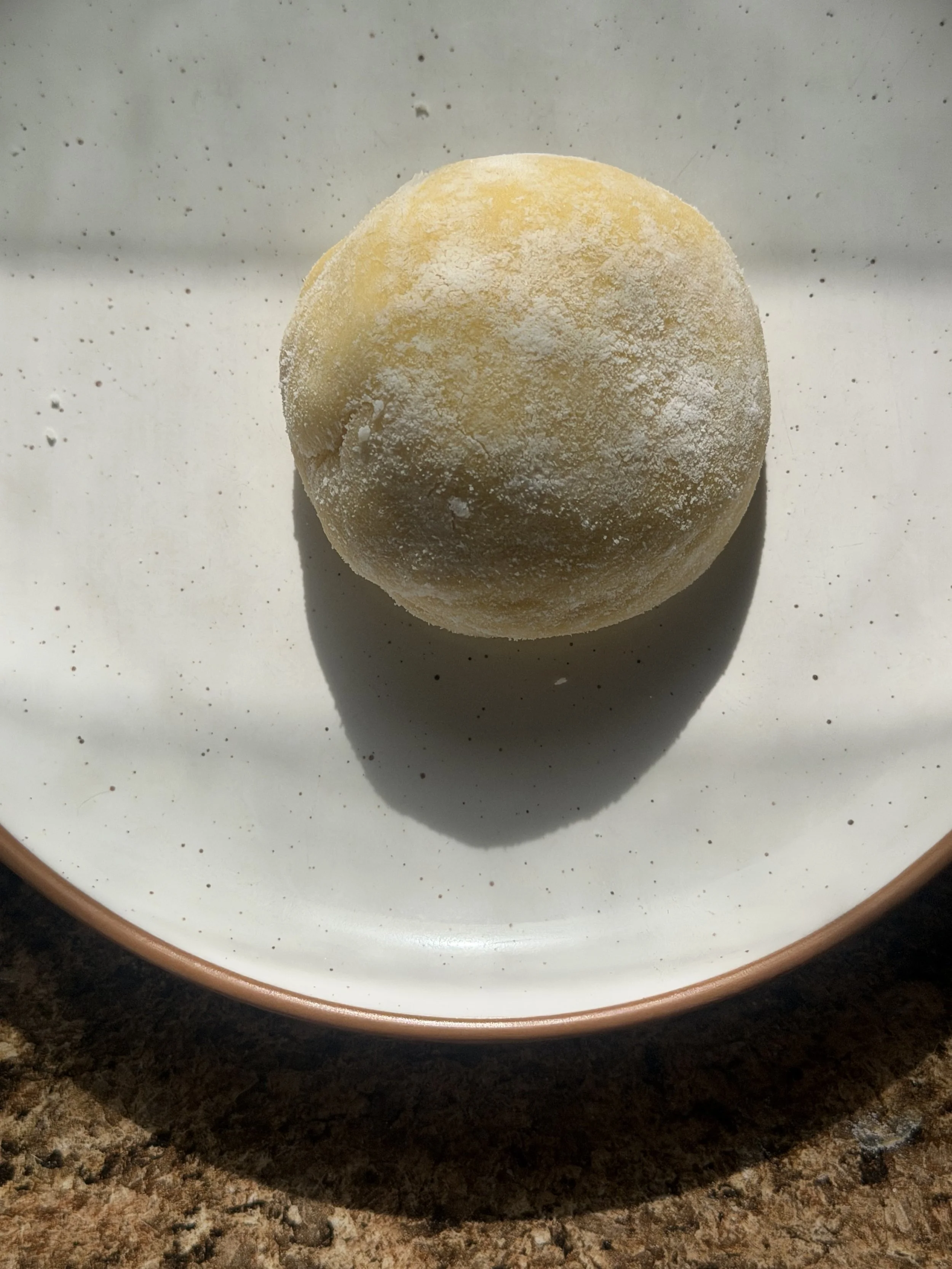 Refined sugar–free Korean tangerine mochi dusted with white rice flour on a ceramic plate, sunlit and ready to bite, offering a chewy citrus dessert that supports gut and skin health.